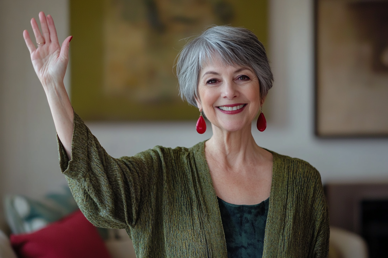A woman in her 60s waving goodbye in a living room with a smile | Source: No source