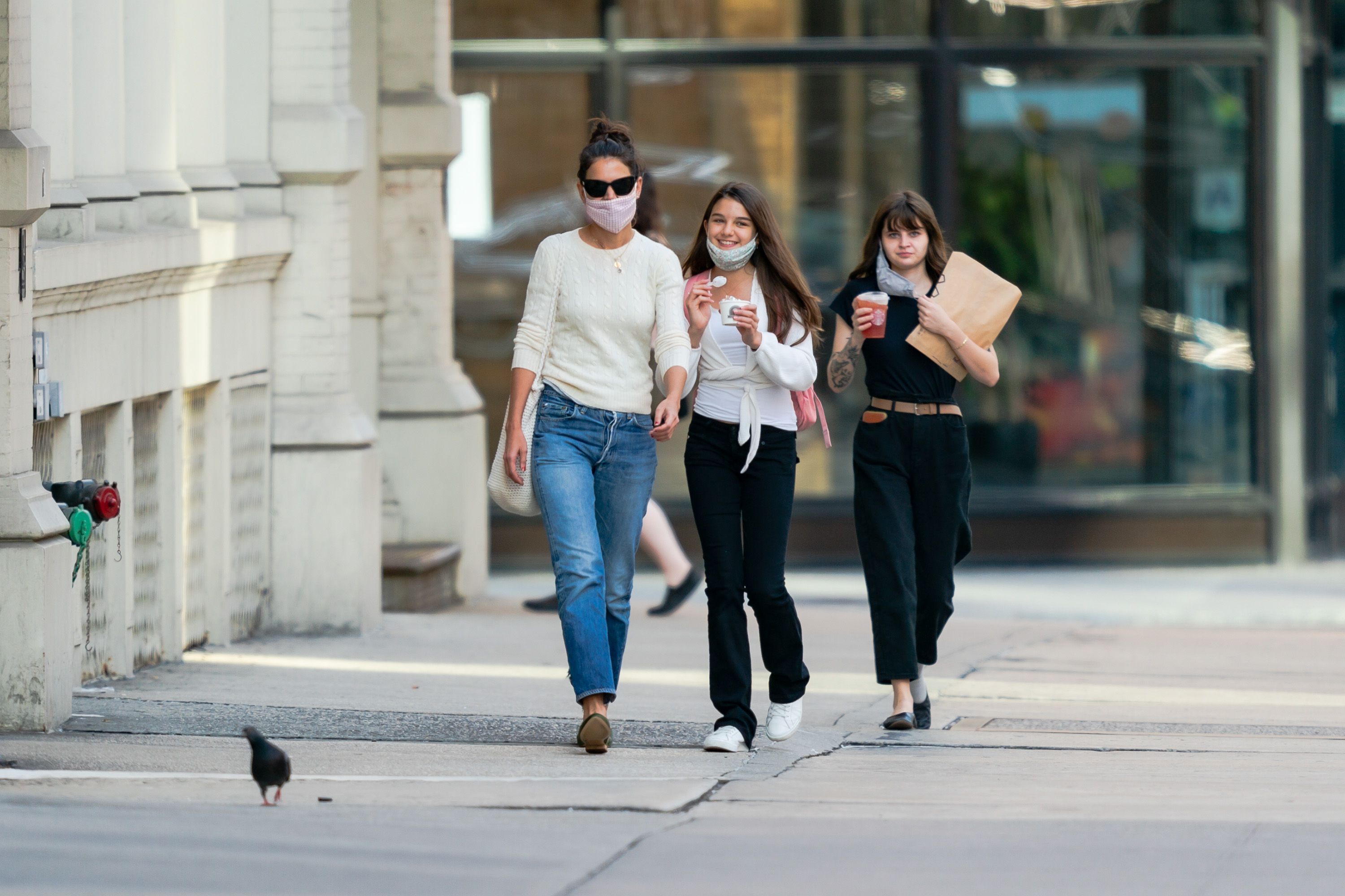 Katie Holmes and her daughter Suri walk side by side against the city backdrop. With matching relaxed confidence and casual elegance, they share a lighthearted moment. The photo captures a perfect blend of style, warmth, and the easy joy of togetherness.