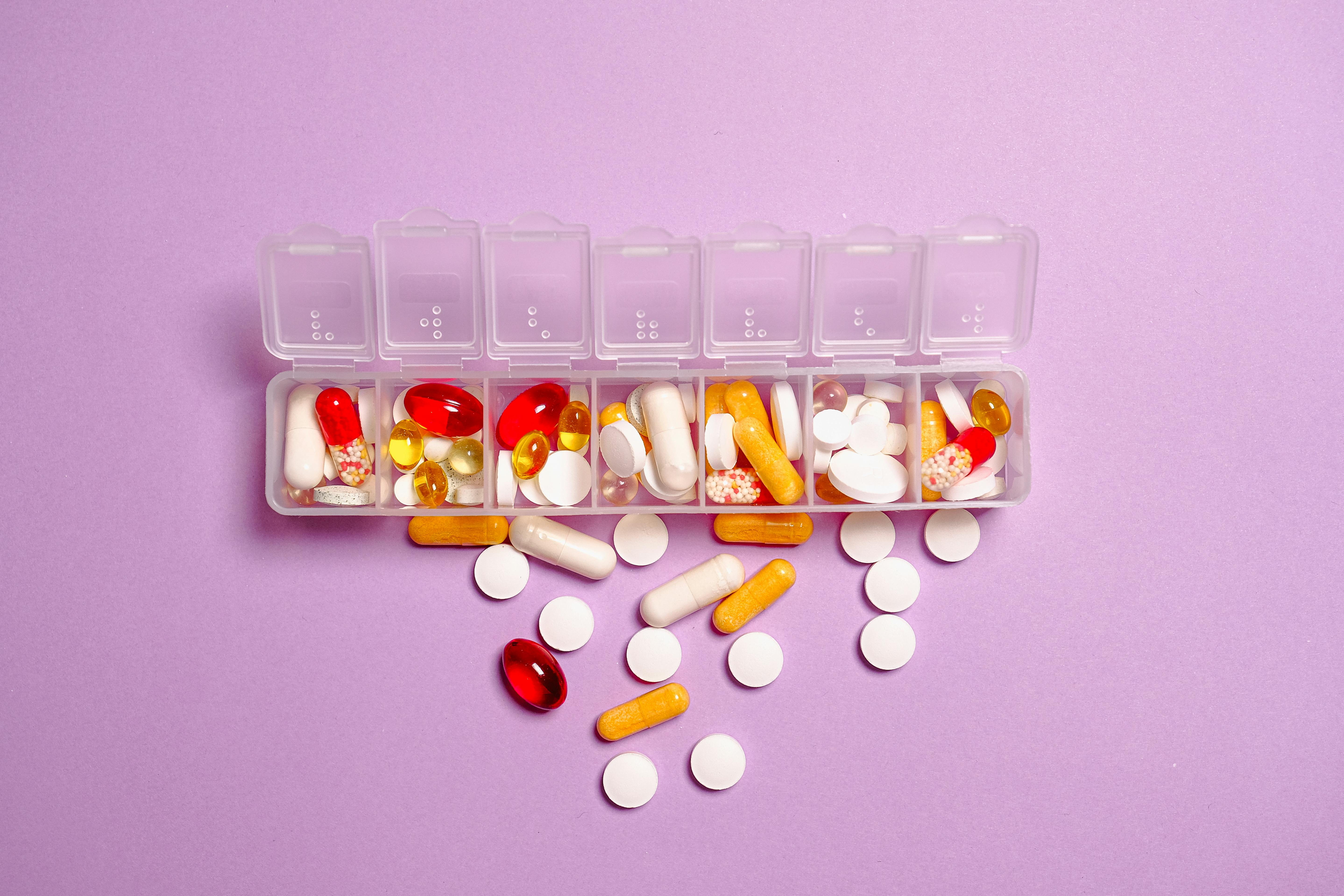 Colorful pills organized in a weekly pill box on a purple background | Source: Pexels