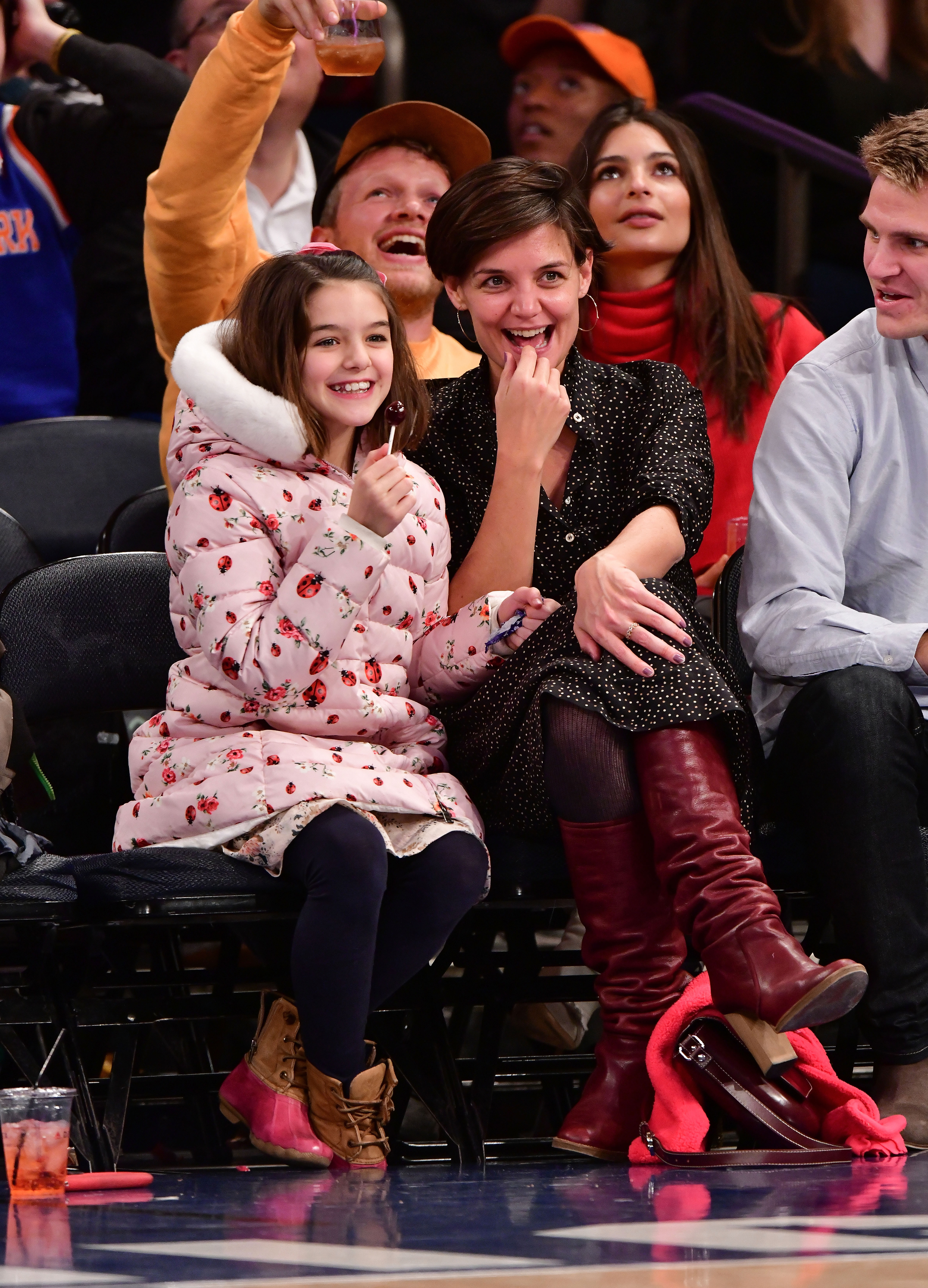 Katie Holmes and Suri share a burst of laughter courtside, their joy brighter than the game itself. Suri, bundled in a pink floral coat, mirrors her mom’s animated excitement. The mother-daughter duo radiates warmth and connection, turning a casual outing into a heartwarming moment.