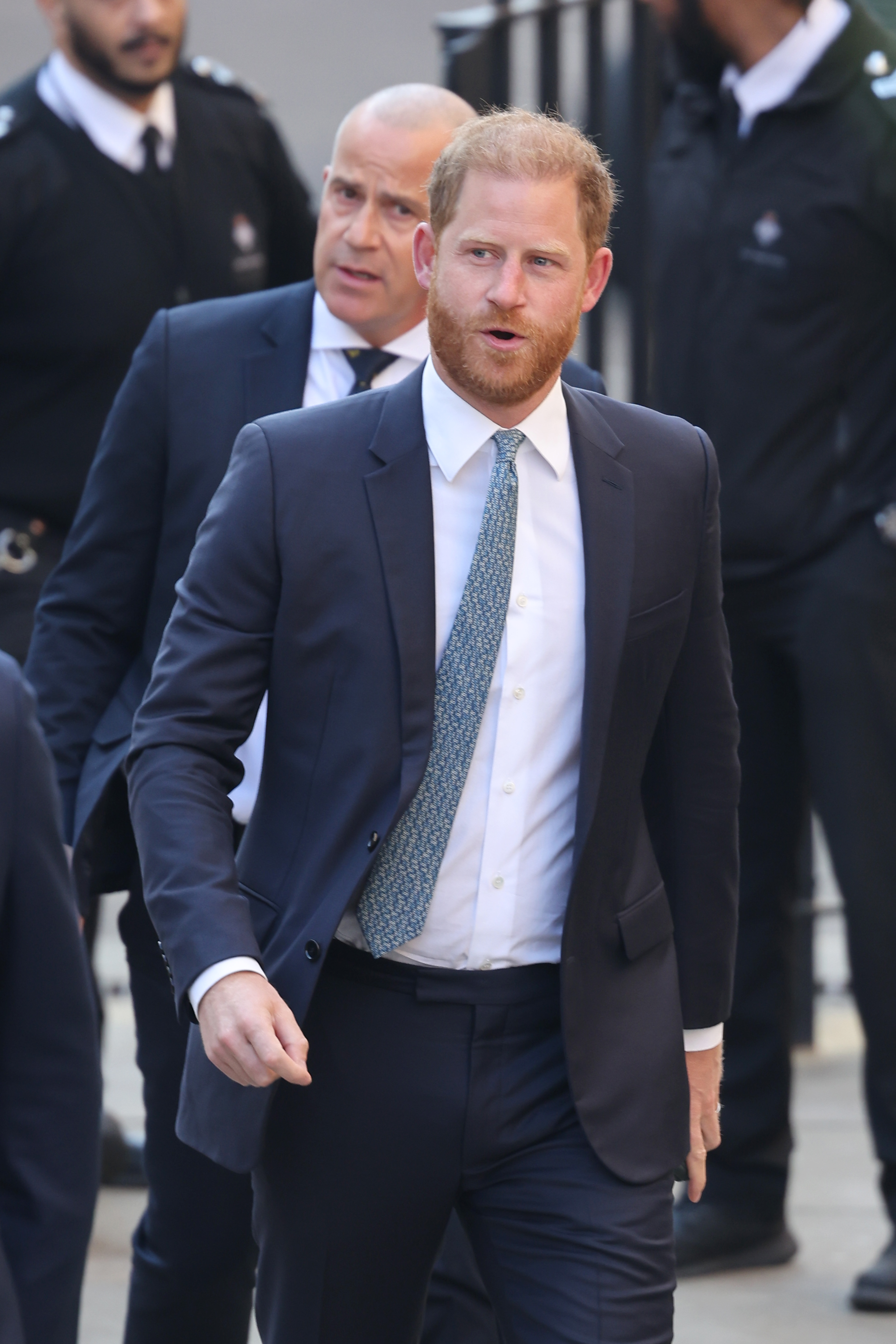 Seen mid-conversation with a member of his security team, Prince Harry walks with a purposeful energy. The royal appears more animated here — his expression one of firm resolve. As he enters the courtroom, the personal stakes behind his appeal become tangible.