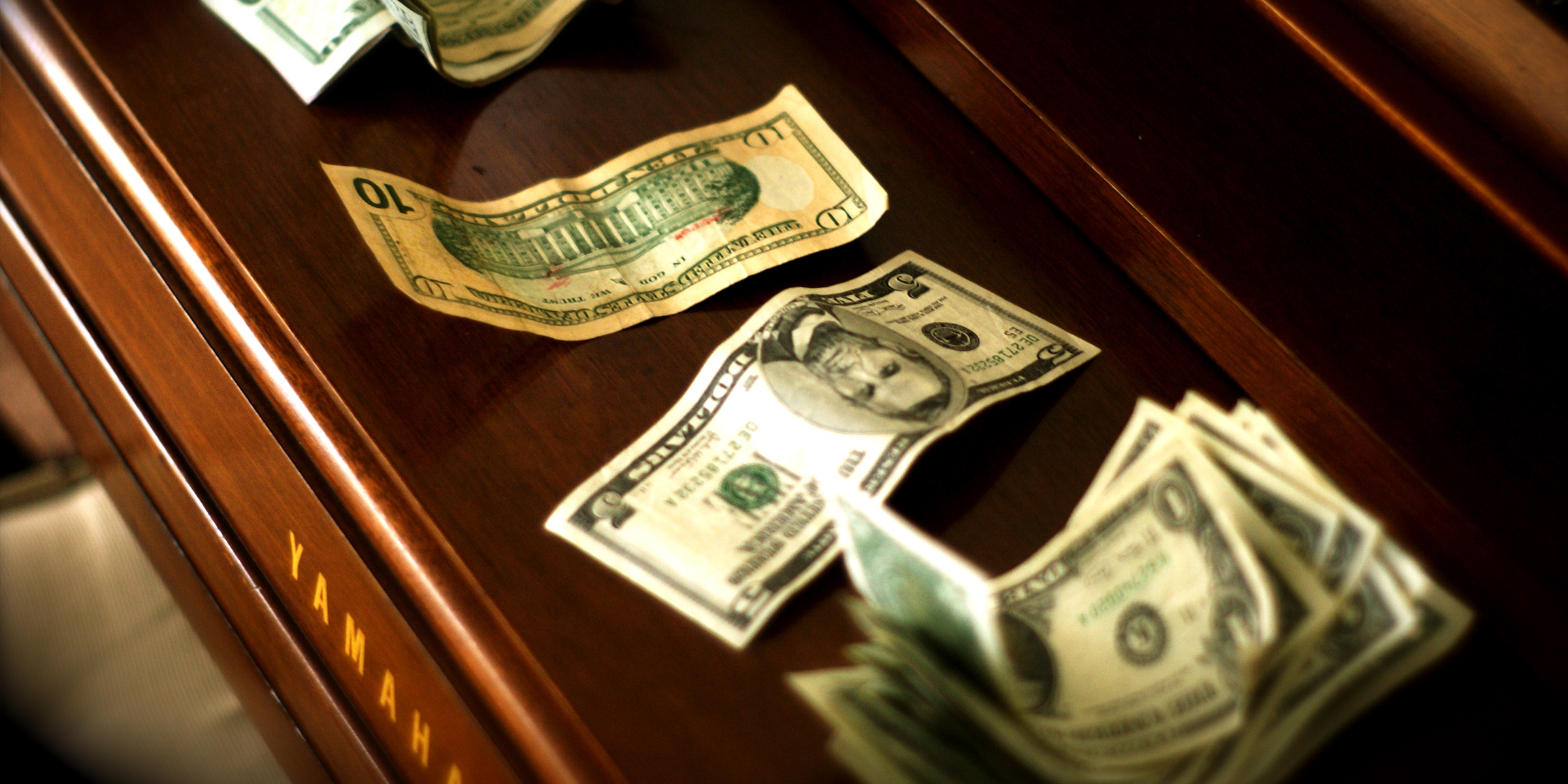 Dollar bills scattered across a polished wooden Yamaha piano | Source: Flickr /Alan / Falcon/CC BY 2.0