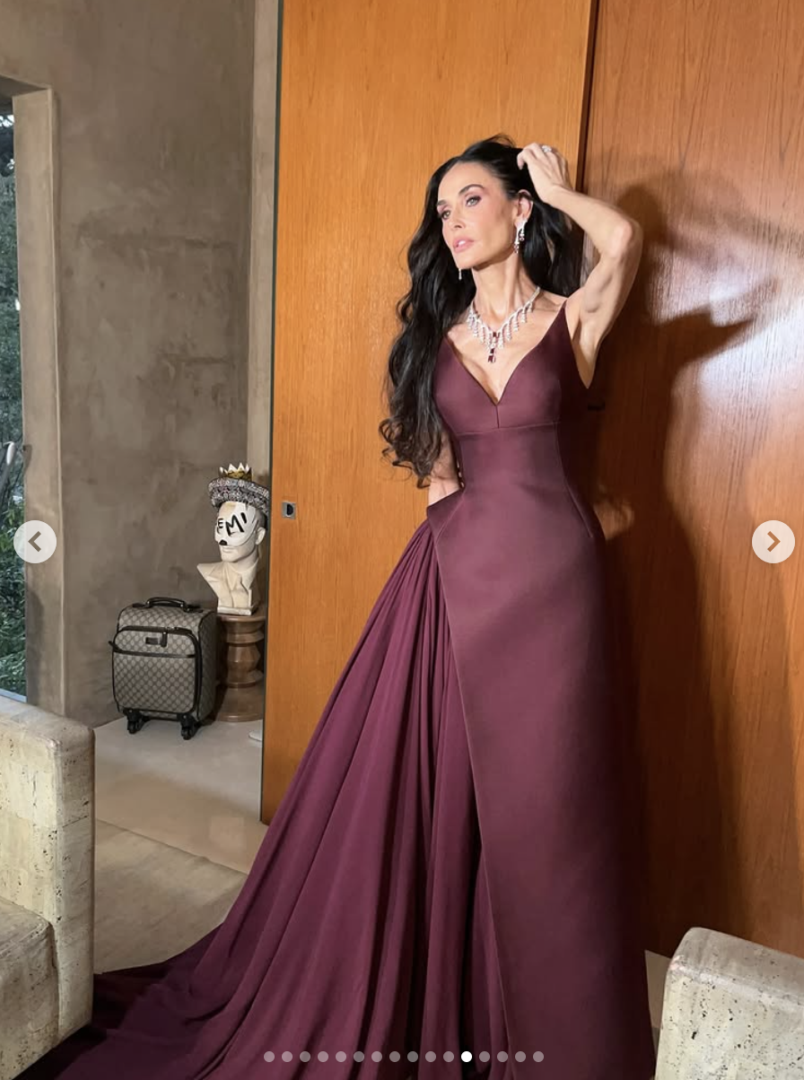 Striking a candid pose against a wood-paneled wall, Demi Moore channels high fashion drama in her flowing maroon gown, one hand sweeping through her hair mid-movement. | Source: Instagram/demimoore