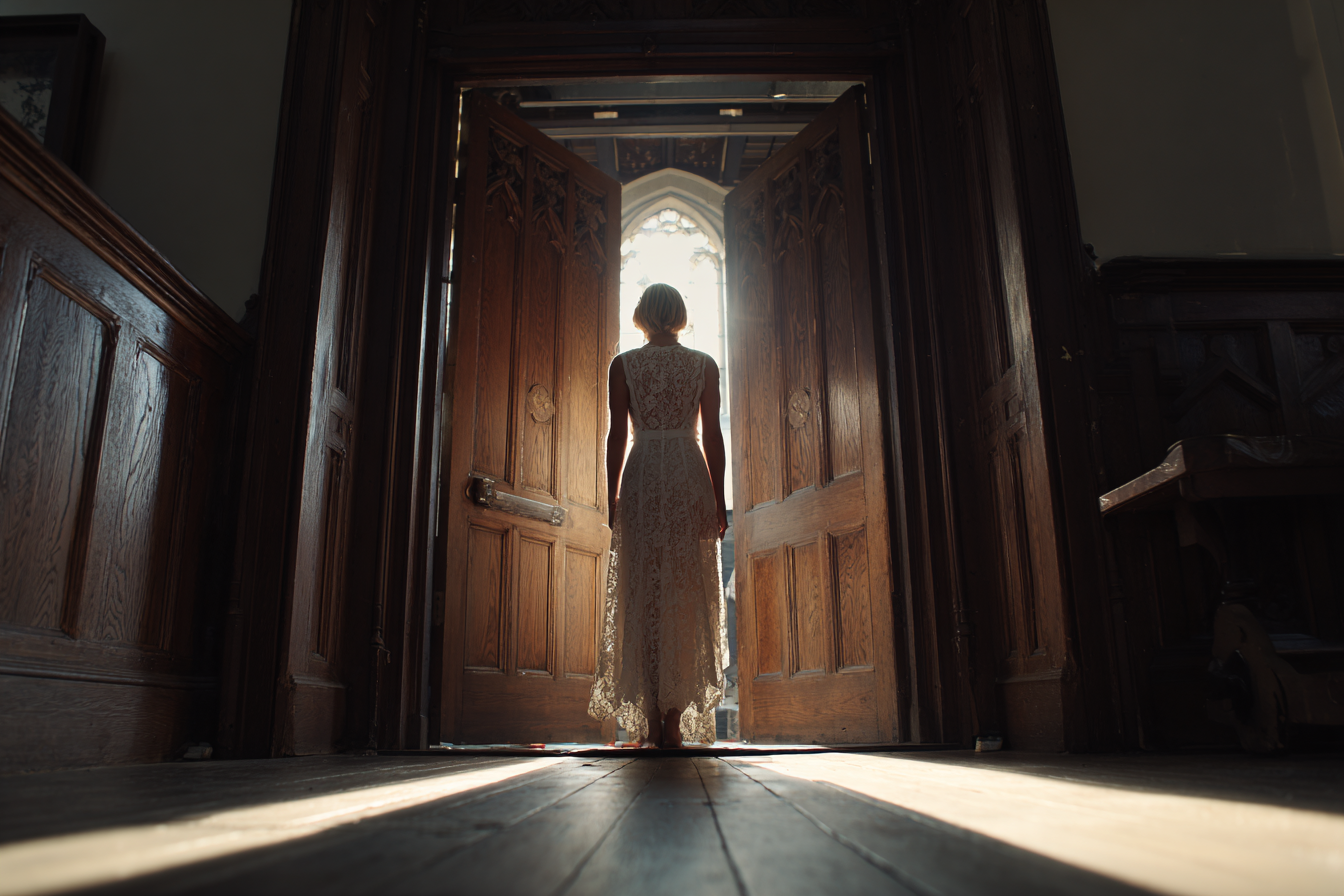 A woman wearing a white lace dress standing in a doorway | Source: No source