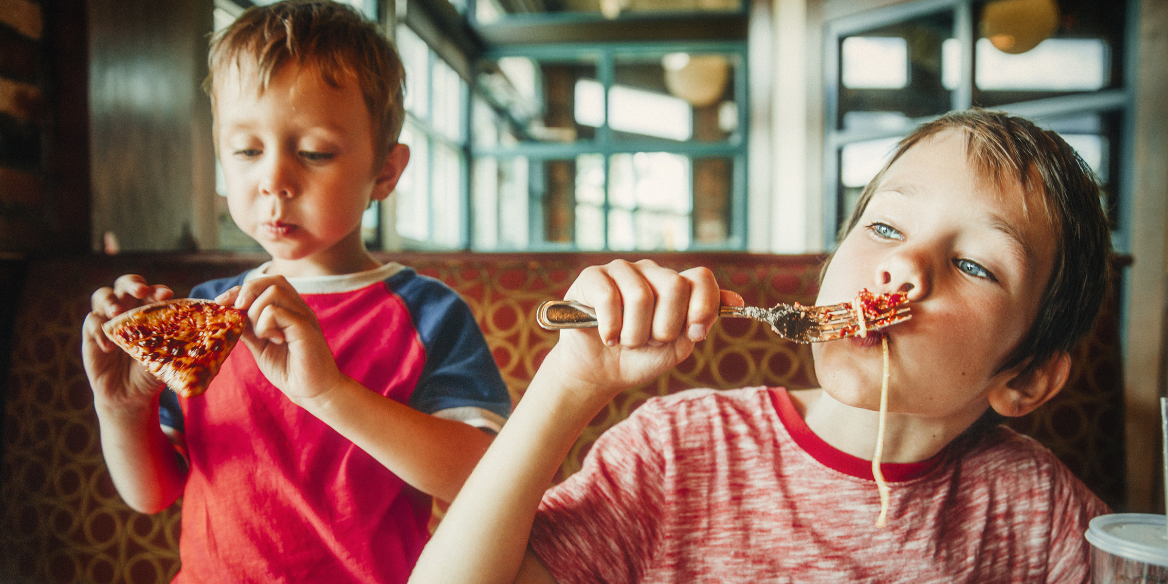 Two kids enjoying pizza and pasta at a restaurant | Source: Shutterstock