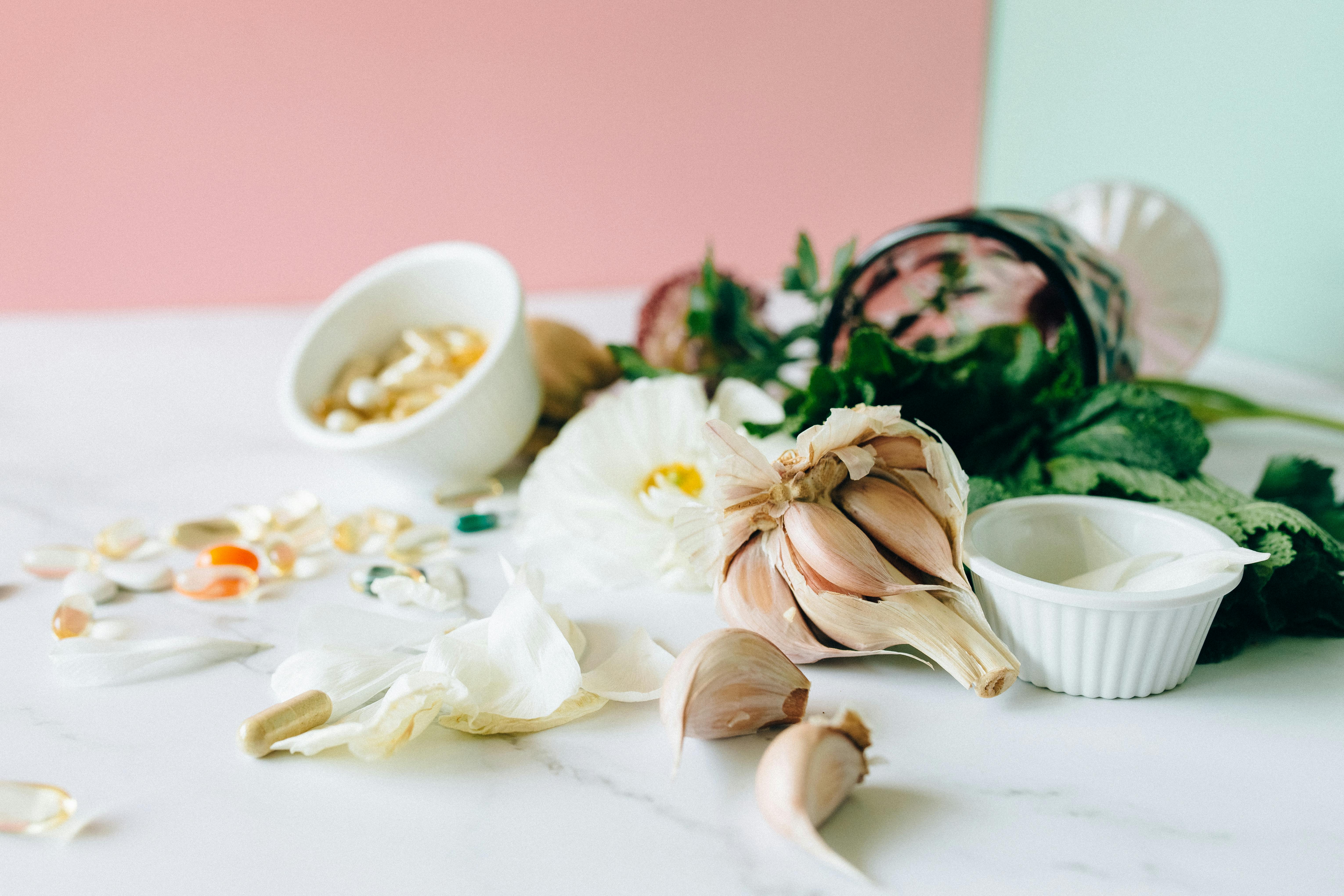 Supplements scattered on a table with garlic and herbs in the background | Source: Pexels