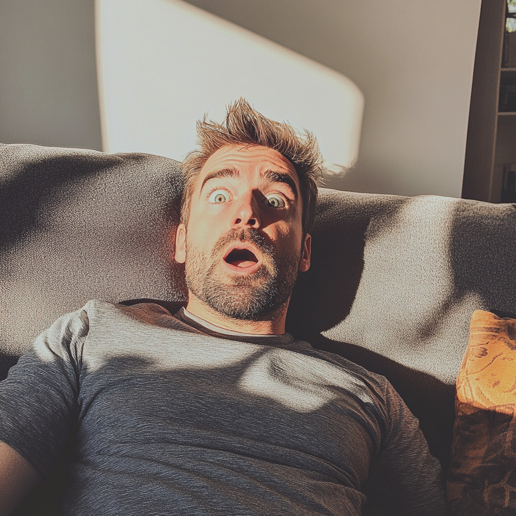 A shocked man sitting on a couch | Source: No source