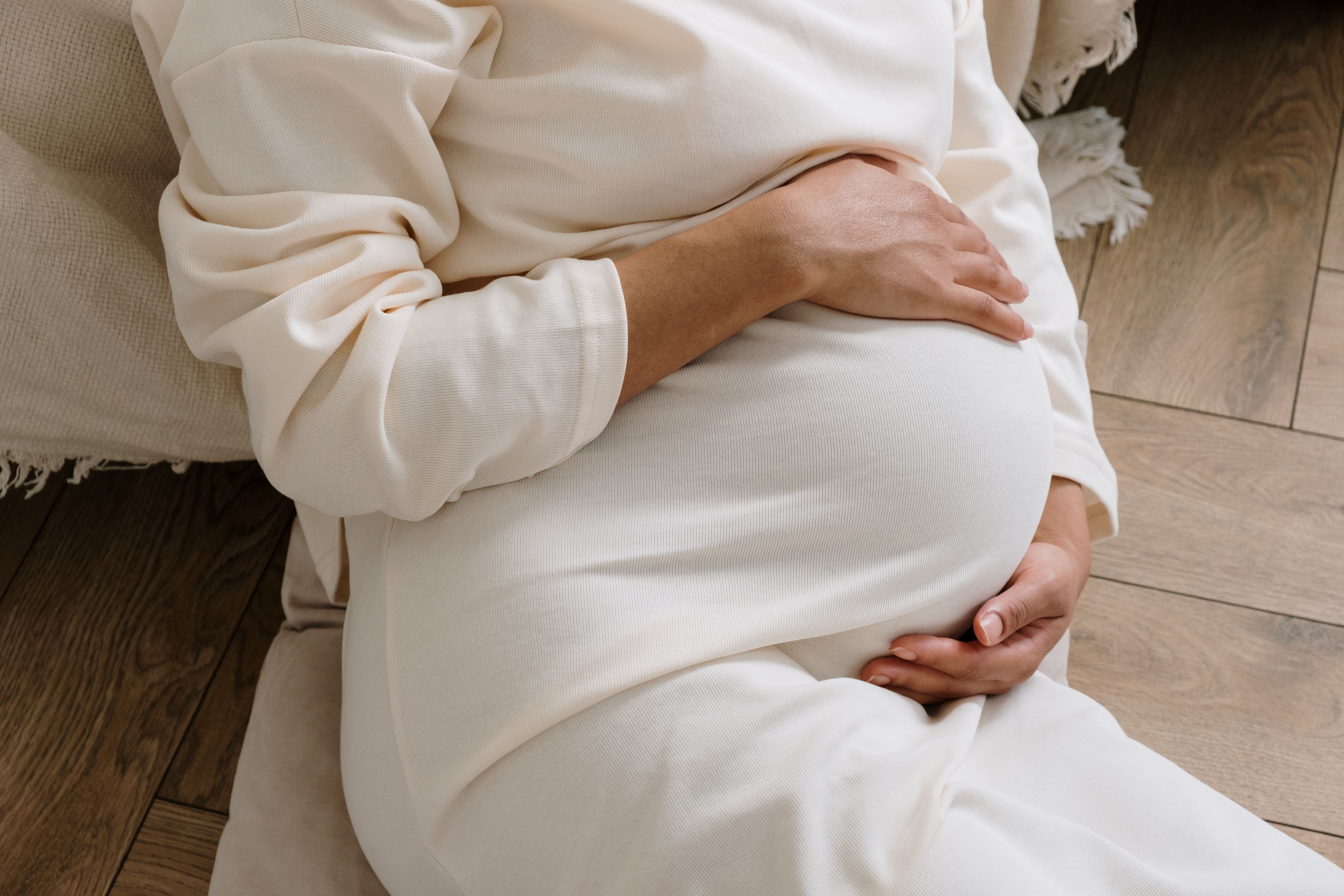 A pregnant woman in a cozy white dress holding her belly | Source: Pexels