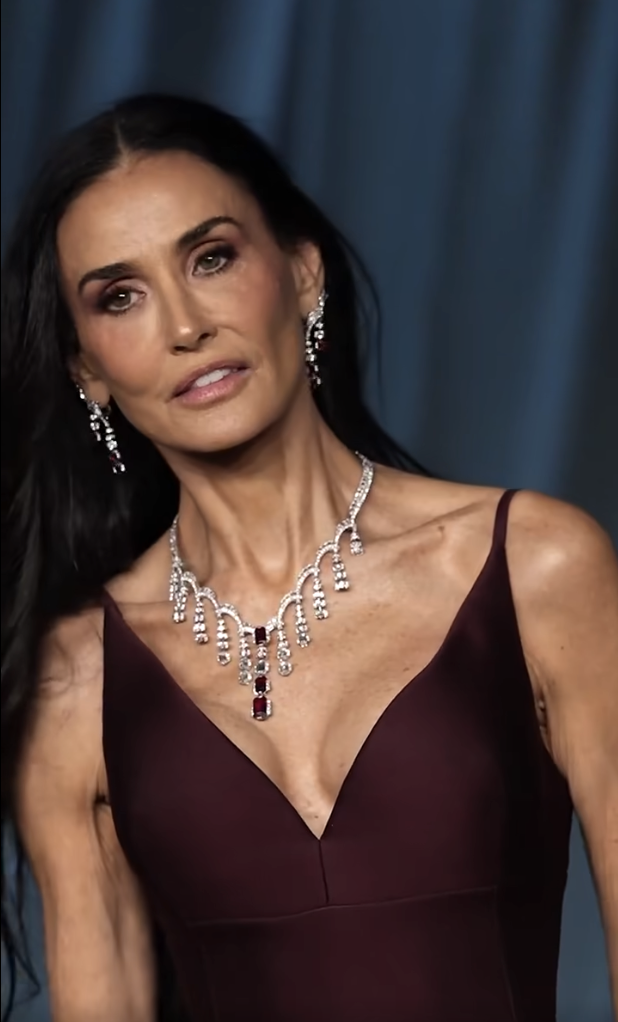 Demi Moore tilts her head ever so slightly, her eyes focused with quiet intensity. She radiates calm control, letting the sharp neckline and ruby-studded diamonds do the talking. | Source: Facebook/TooFab
