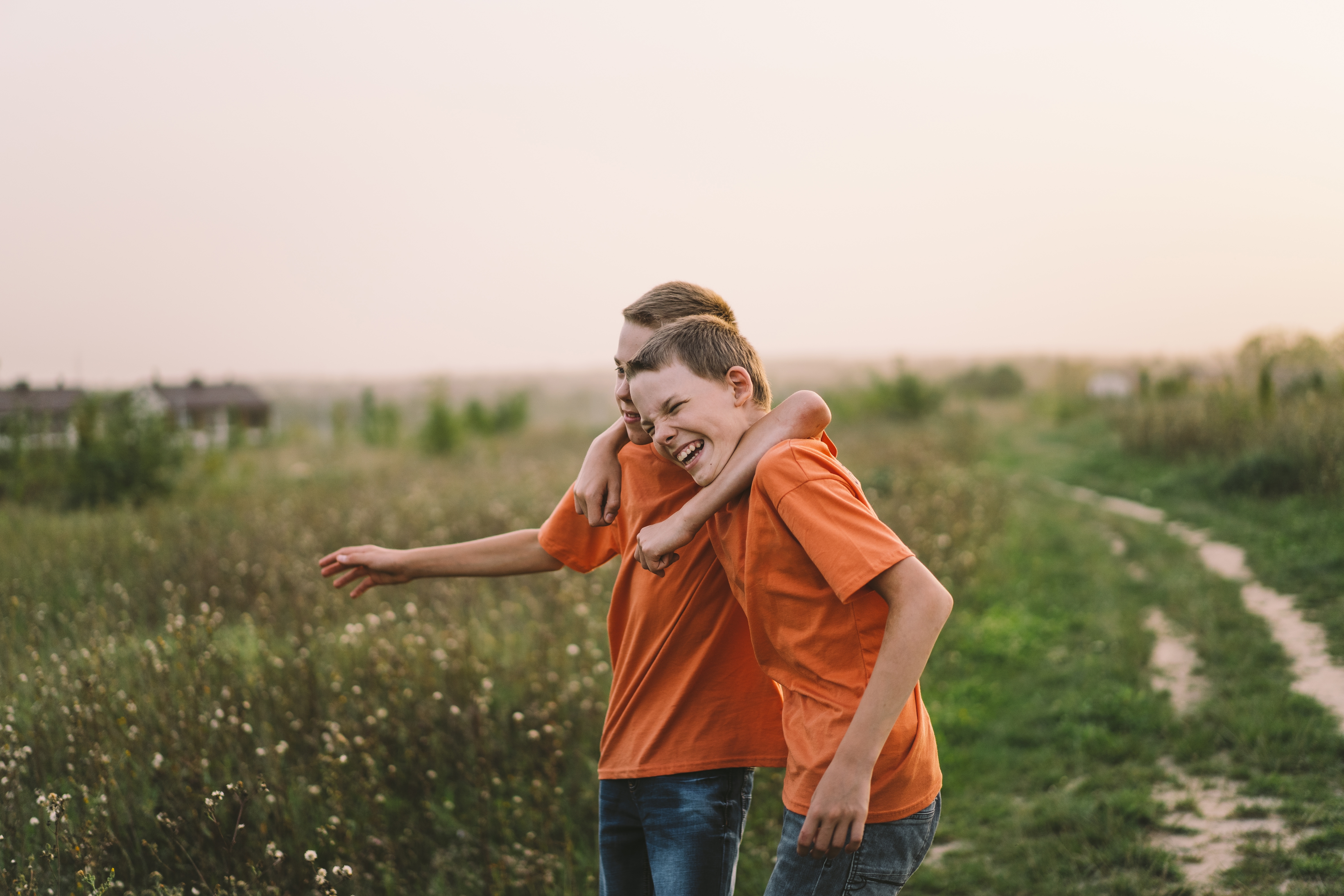 Funny twin brother boys in orange t-shirt playing outdoors on field at sunset | Source: Shutterstock.com