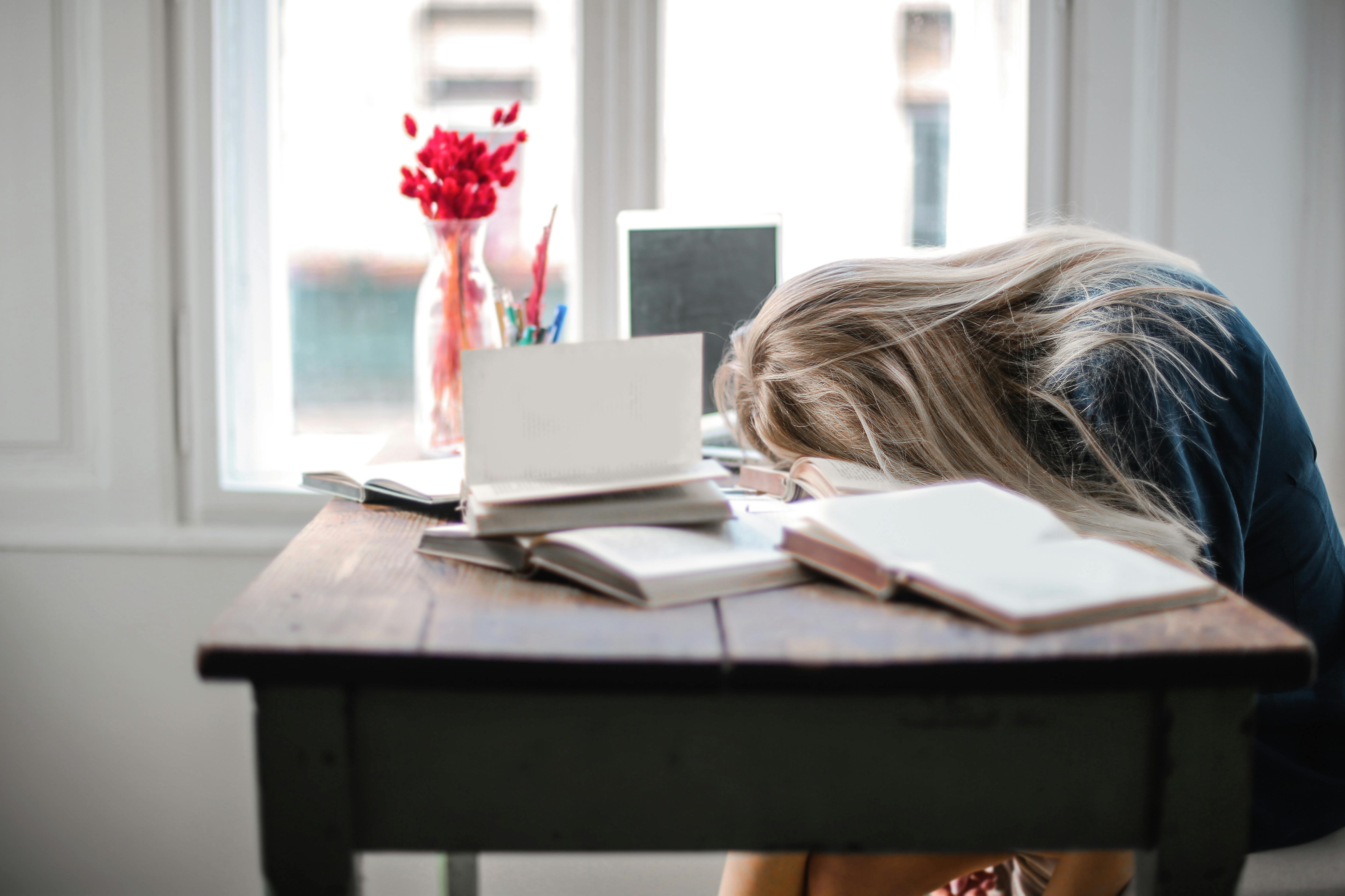 Woman resting on a desk full of open books | Source: Pexels