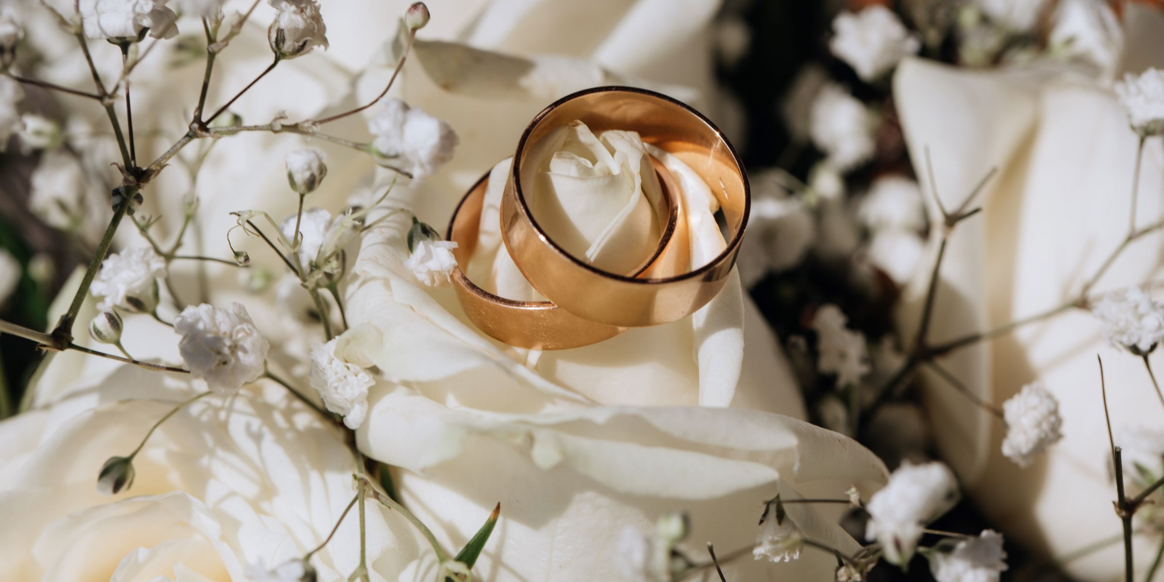 Two gold wedding rings lying among white flowers | Source: No source