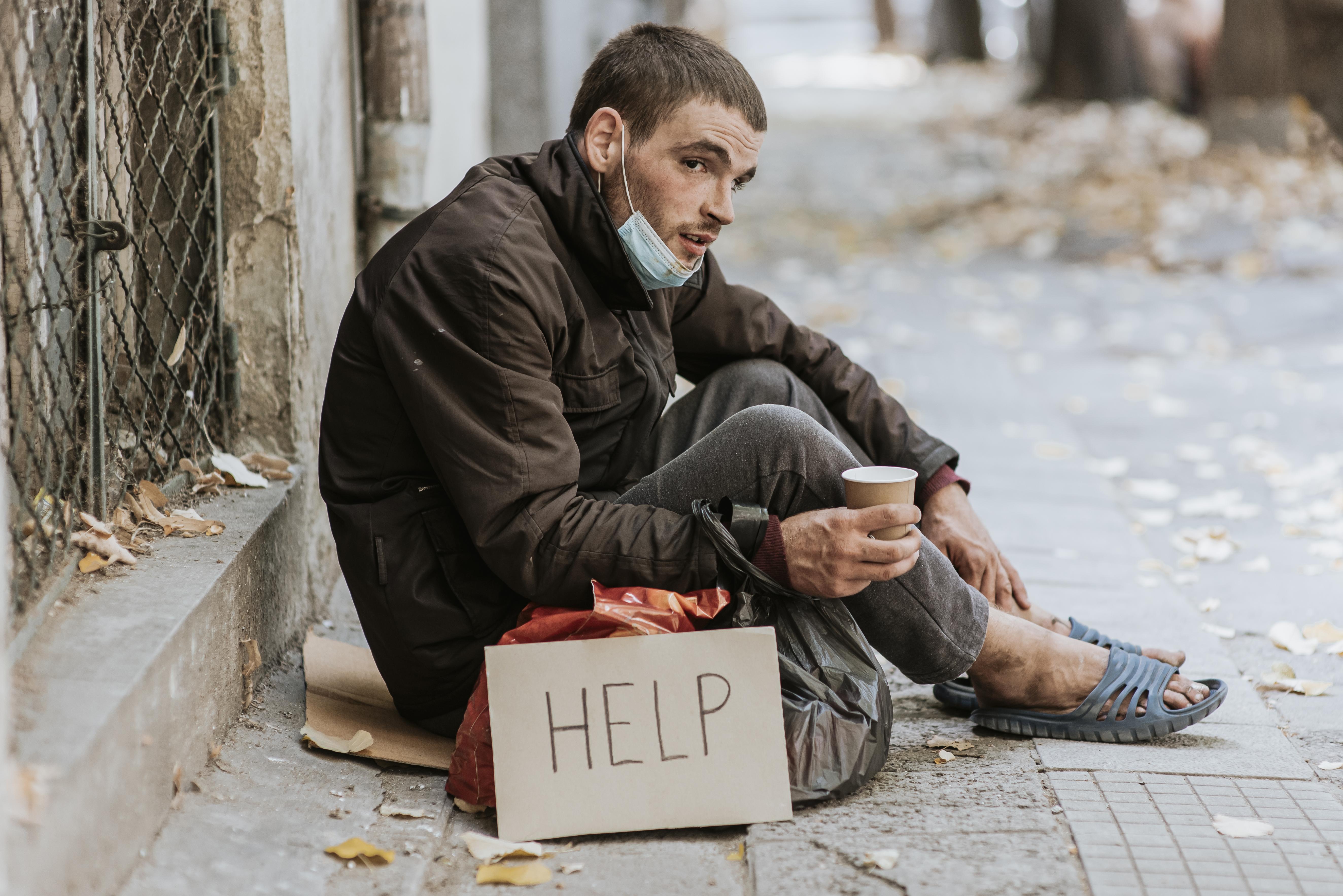 Homeless man sitting on the sidewalk with a help sign and cup | Source: Freepik