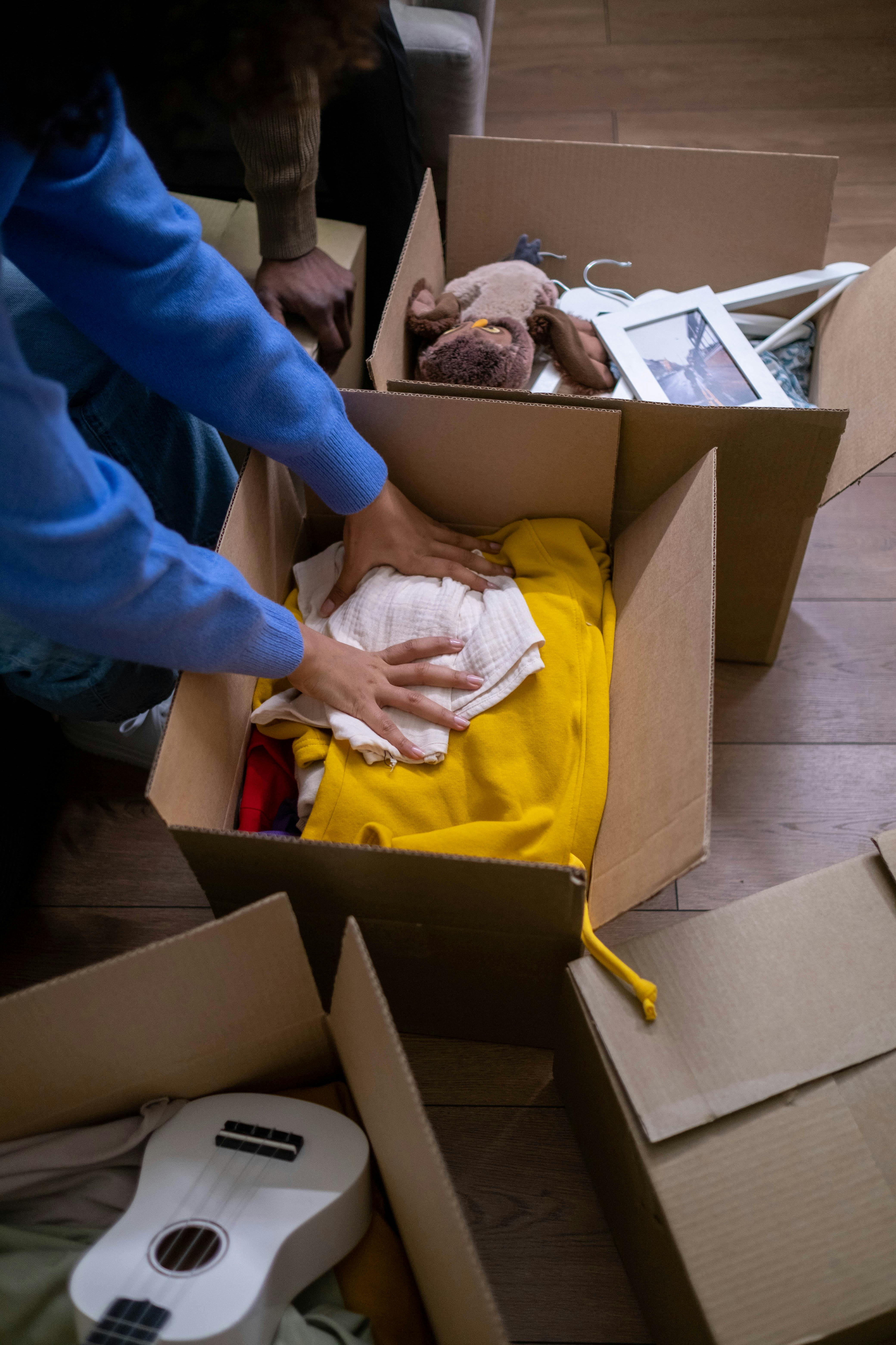 A person packing clothes in a cardboard | Source: Pexels
