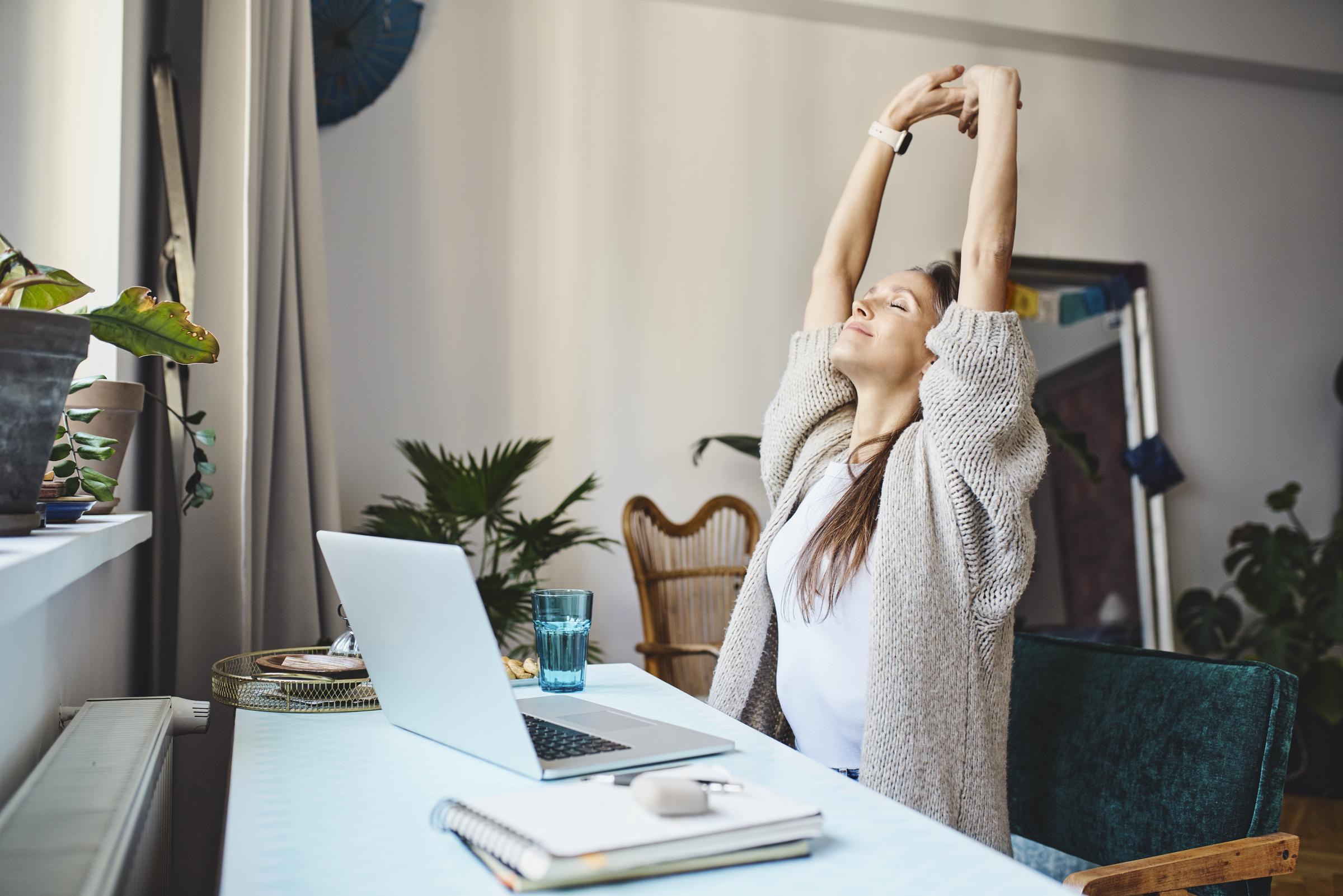 A woman stretching at her desk | Source: Getty Images
