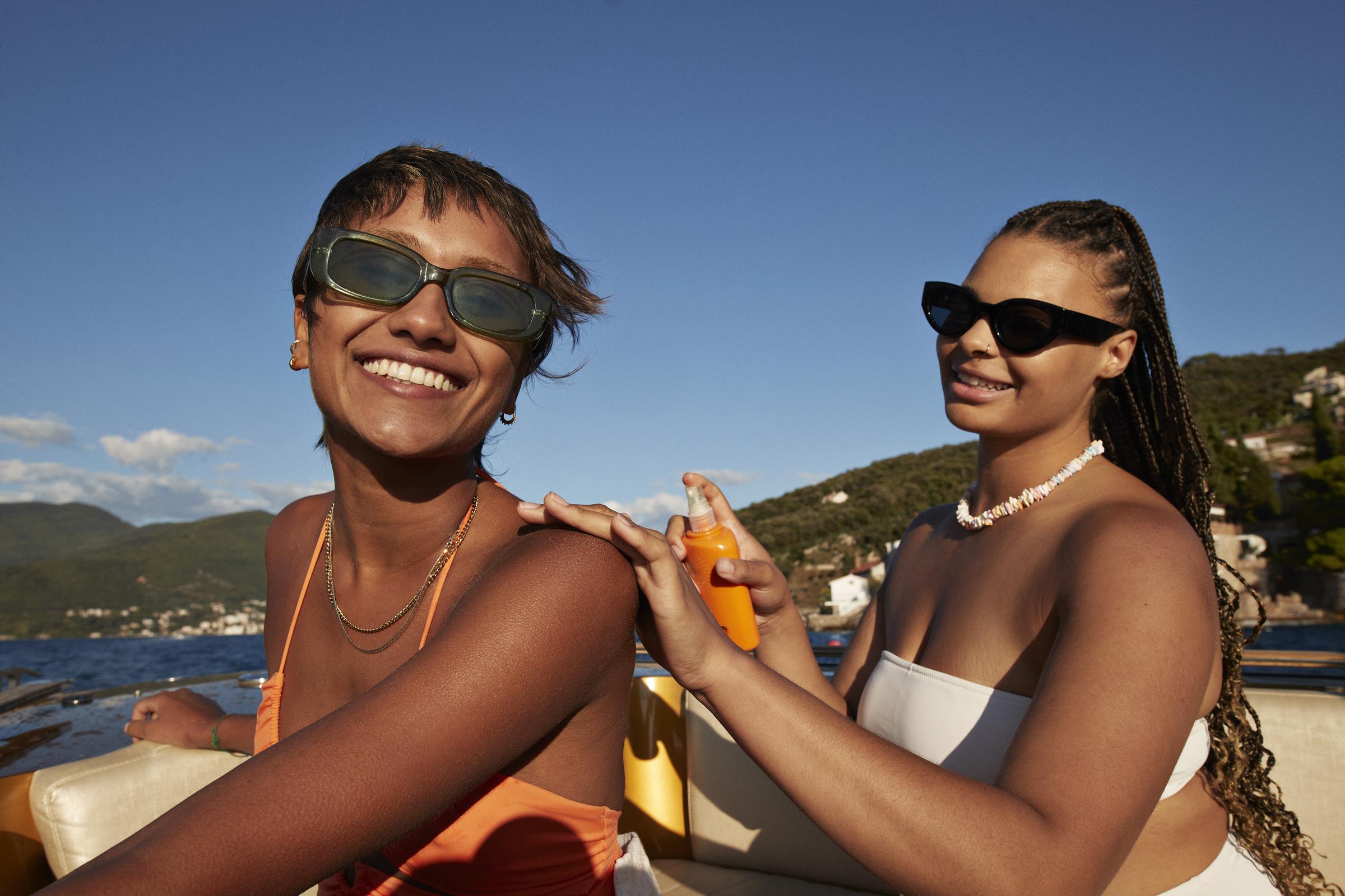 A young woman applying sunscreen on her friend's back | Source: Getty Images
