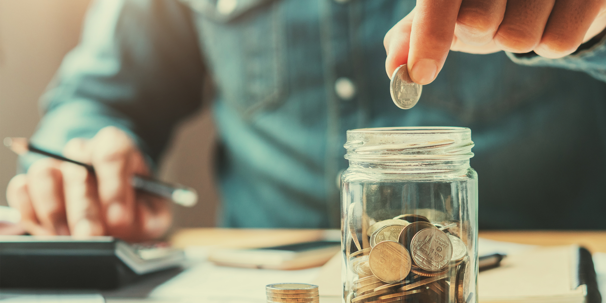 Hands placing coins in a glass while calculating expense | Source: Shutterstock