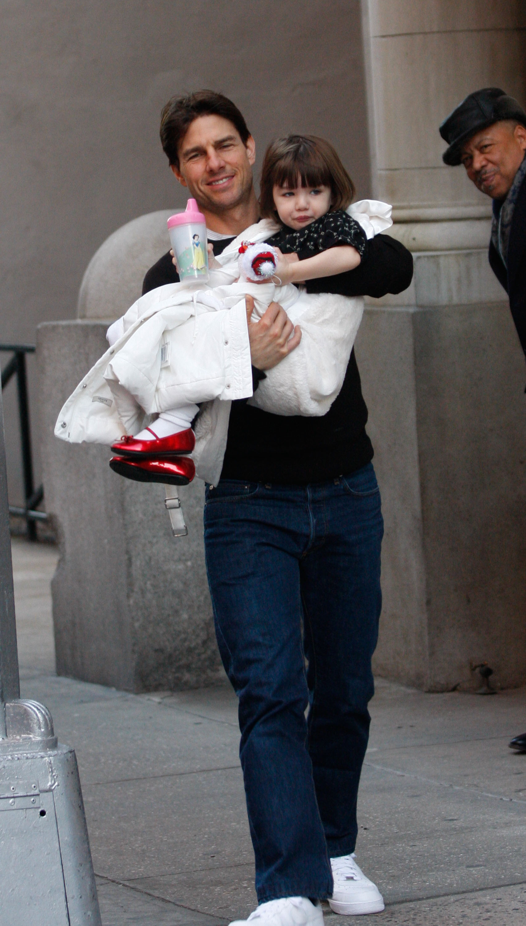 Tom Cruise walks with a proud smile, carrying little Suri gently in his arms through the city streets. Dressed in cozy layers and bright red shoes, she clings to her cup, safe in her father’s embrace. Their candid moment radiates warmth and a tender snapshot of love beyond the spotlight.