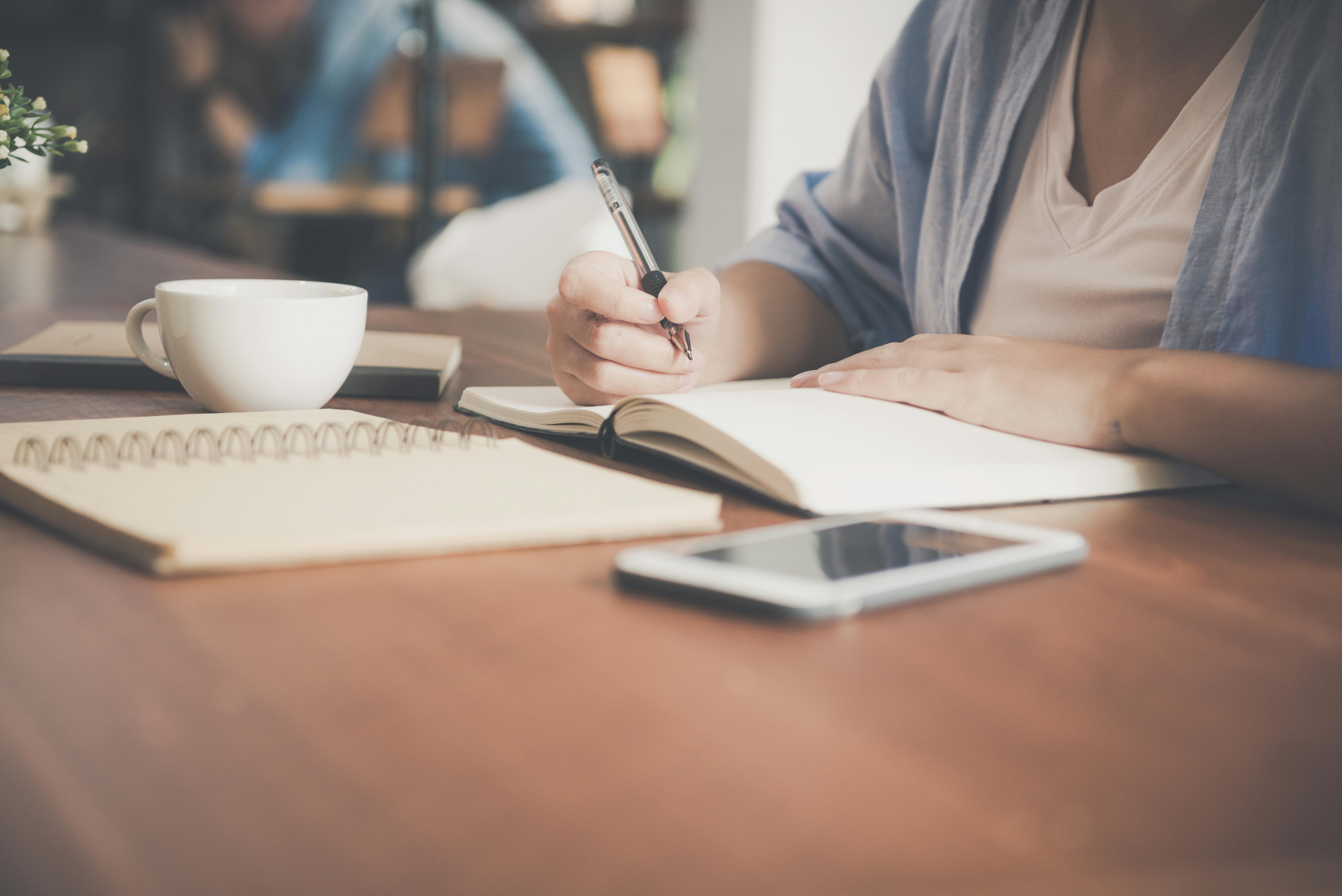 A woman writes on a laptop next to a cup and a tablet | Source: Pexels