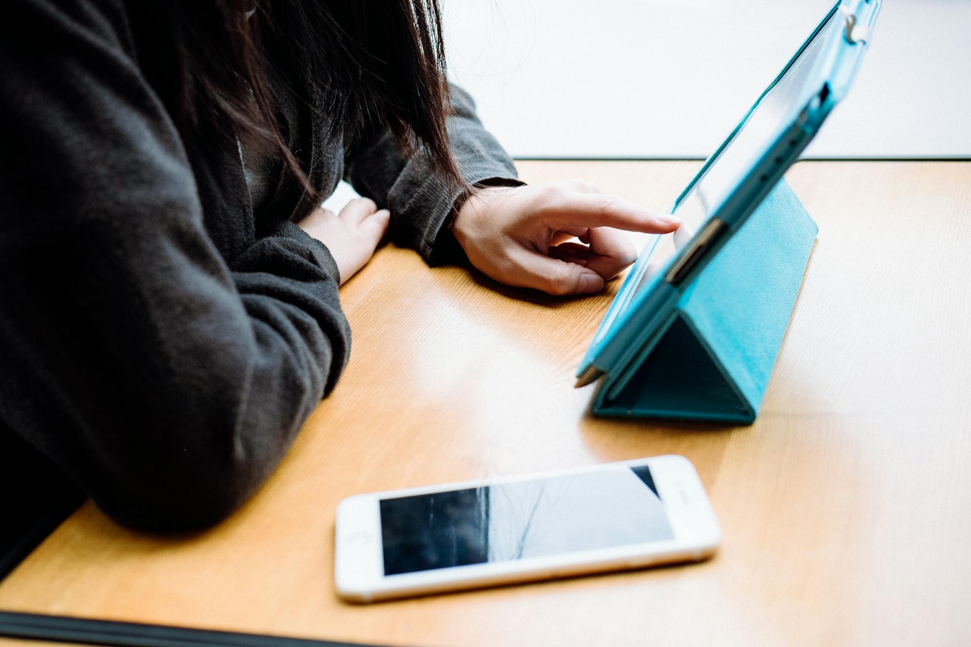 A woman using a tablet while her phone is on the table | Source: Pexels
