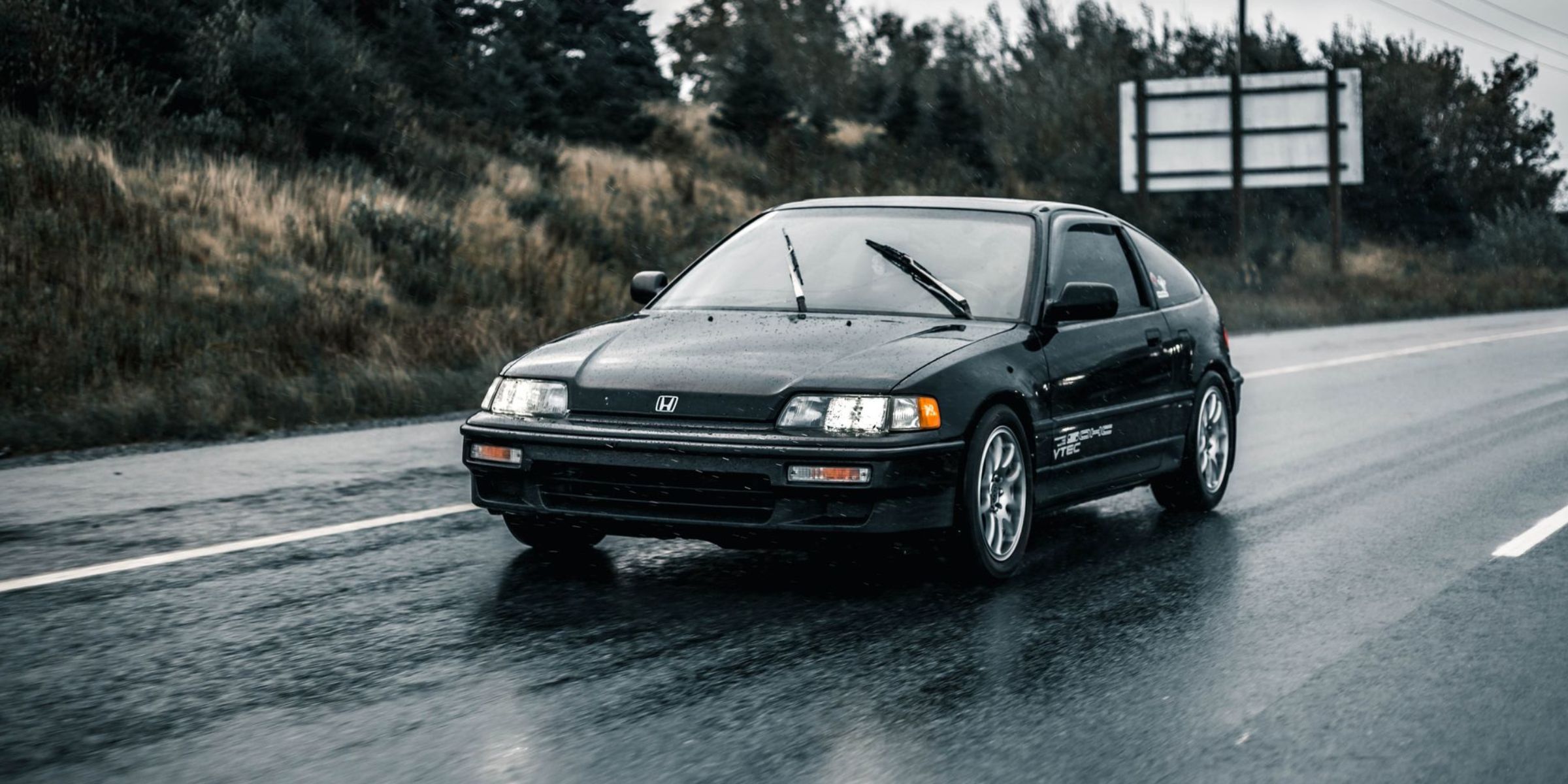 A black car driving along a rain-soaked road with headlights reflecting off the wet pavement | Source: Pexels