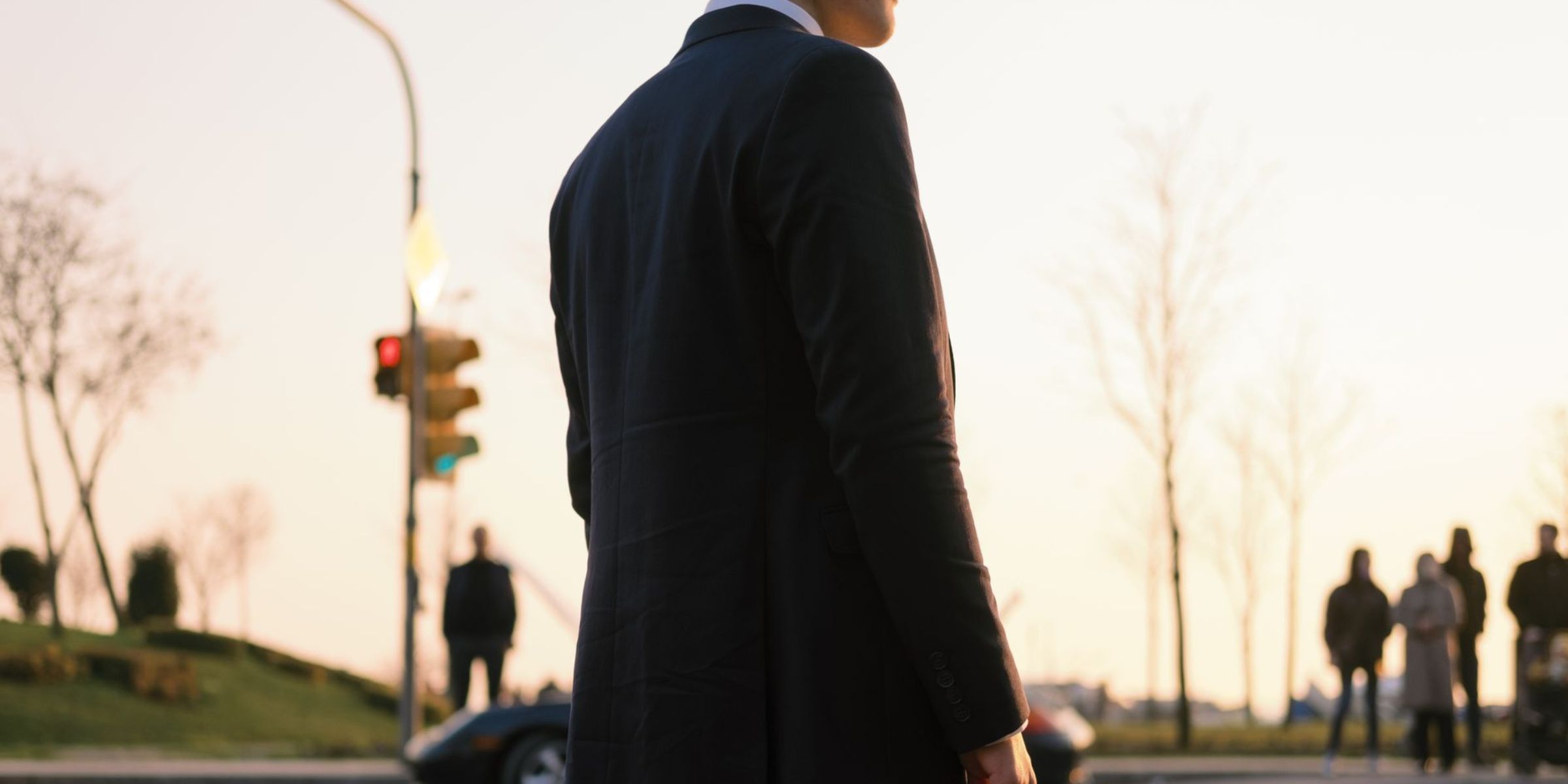 A man in a suit standing alone as people gather in the distance | Source: Pexels