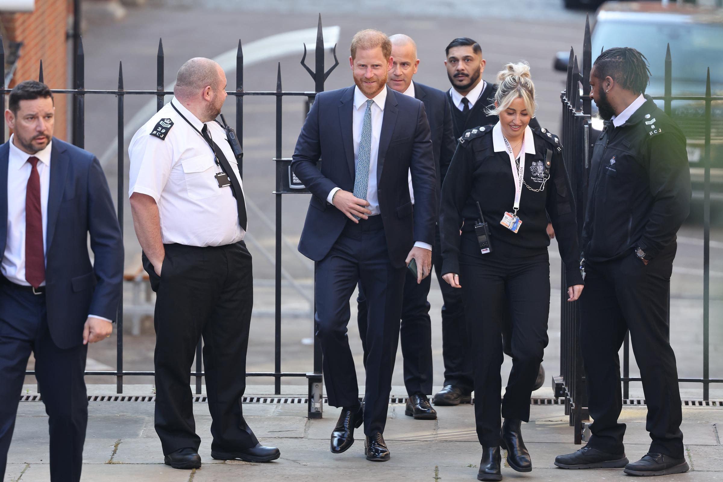 Flanked by both suited aides and uniformed officers, Prince Harry appears momentarily at ease as he engages with members of his security detail outside the courthouse gates. Behind the scenes, the legal complexities he faces span nearly four years, with no resolution yet in sight.