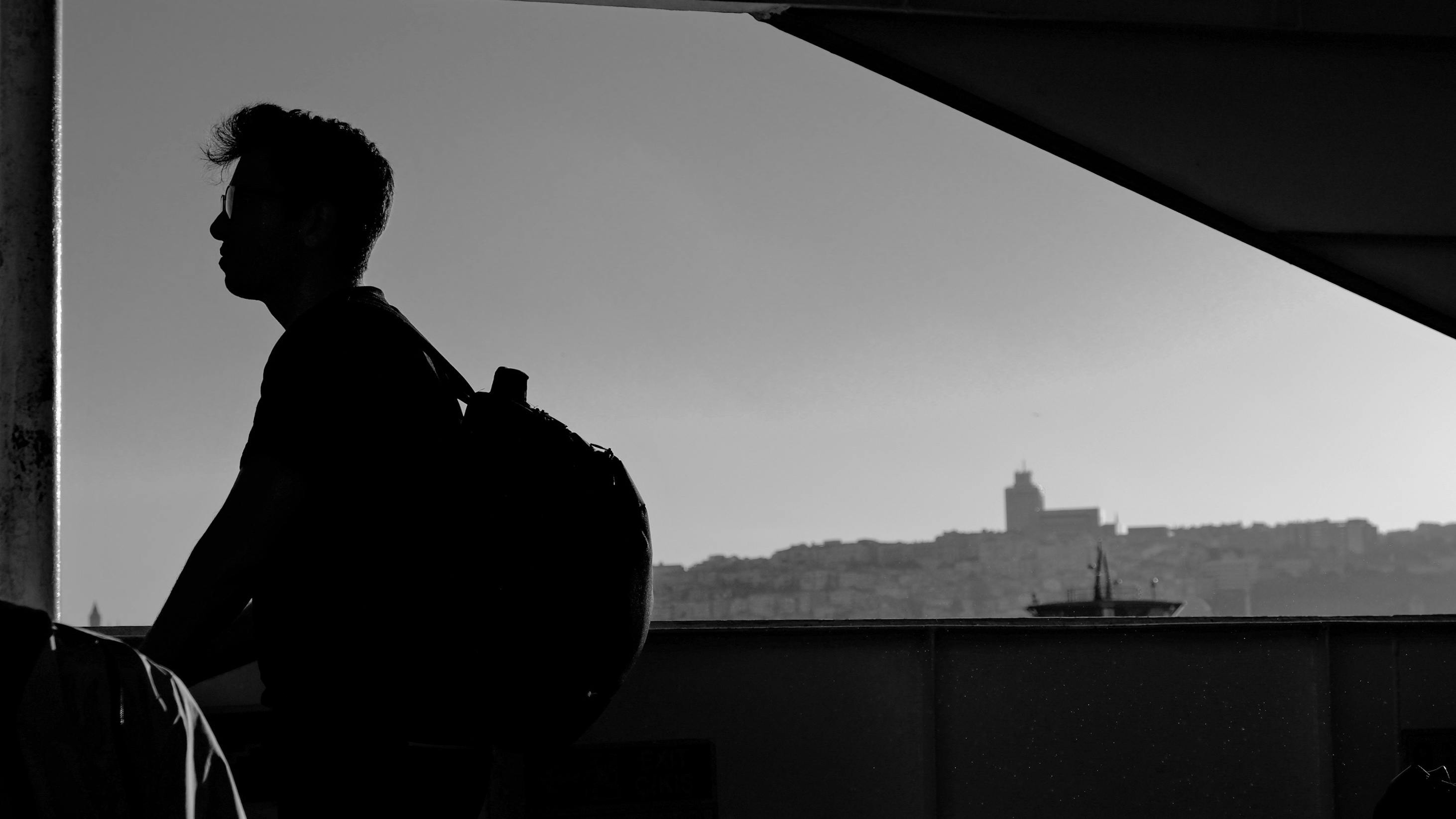 A man with a backpack stands in silhouette, gazing pensively toward the horizon. | Source: Pexels