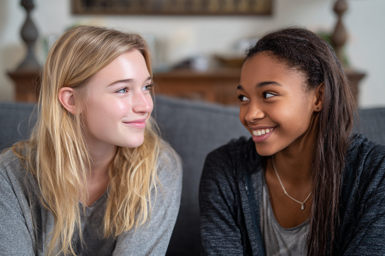 Two teen girls smiling at each other on a sofa | Source: No source
