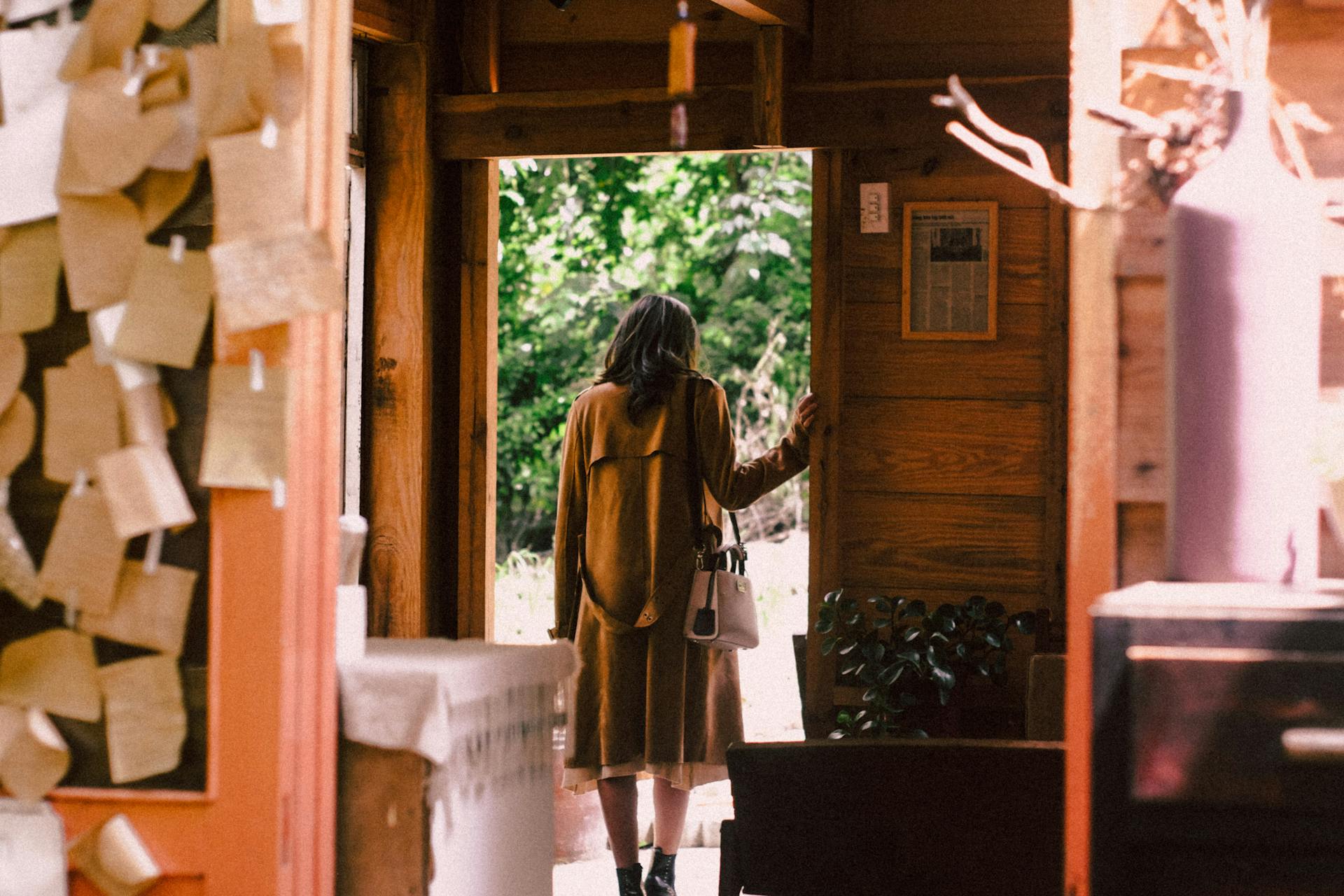 A woman in a long brown coat and boots leaving a house | Source: Pexels