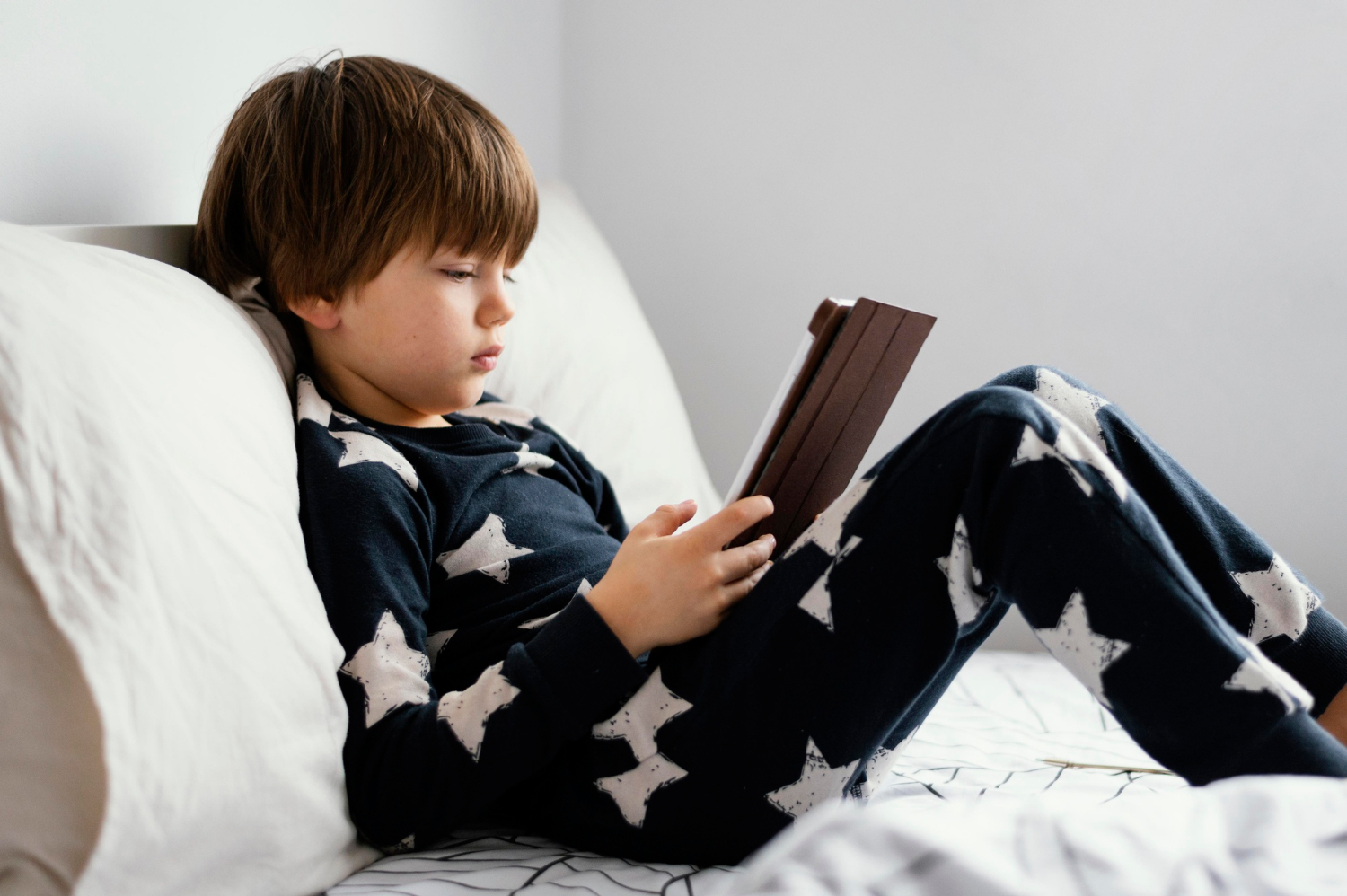 A boy sitting on the bed with his digital tablet | Source: Freepik