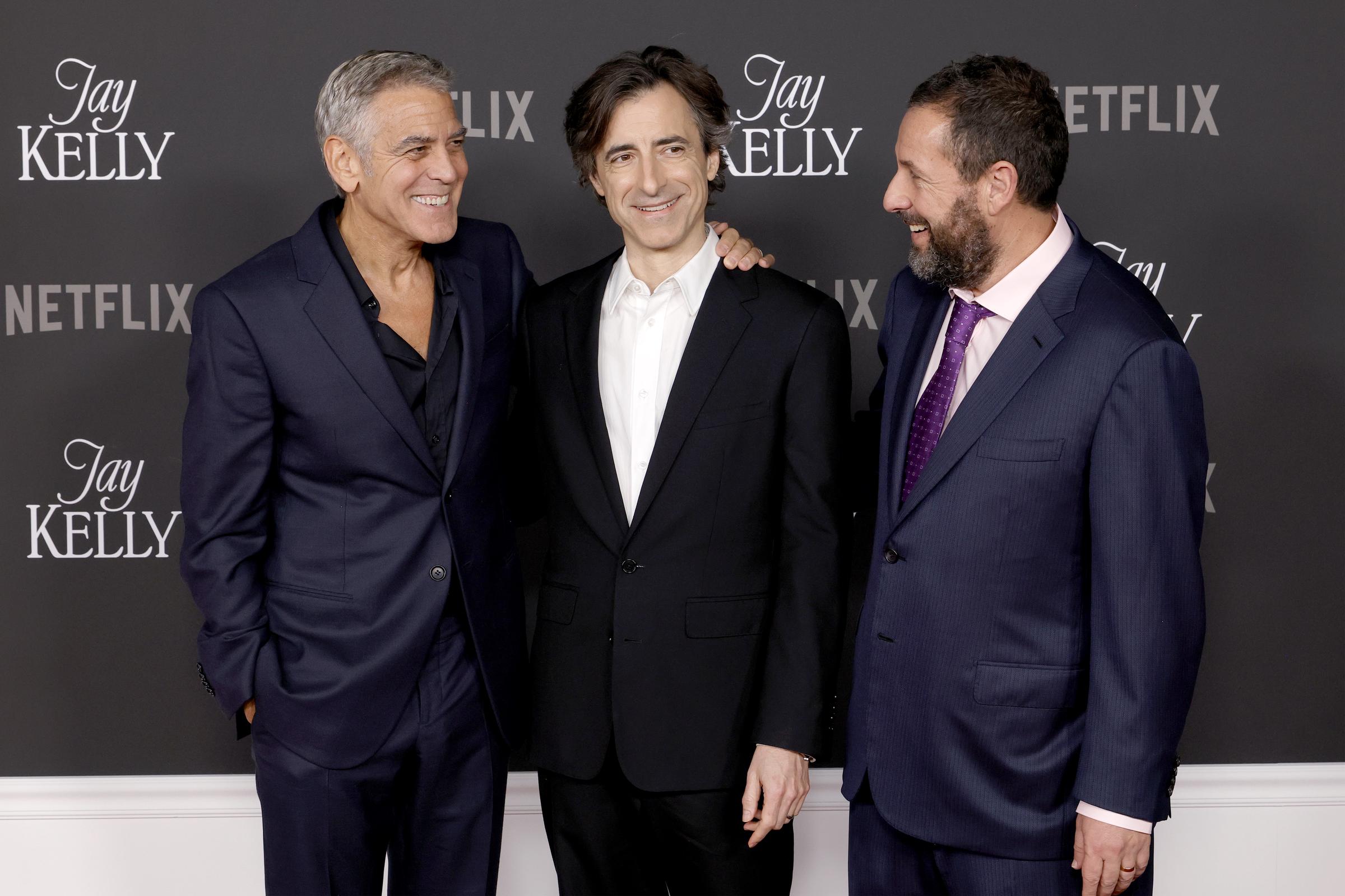George Clooney, Noah Baumbach, and Adam Sandler share a moment of pure joy and pride as they laugh together on the red carpet at the premiere of the film they star in, "Jay Kelly."