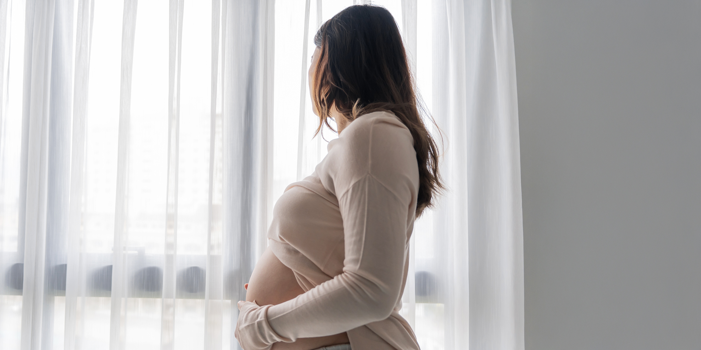 A pregnant woman looking outside a window | Source: Shutterstock