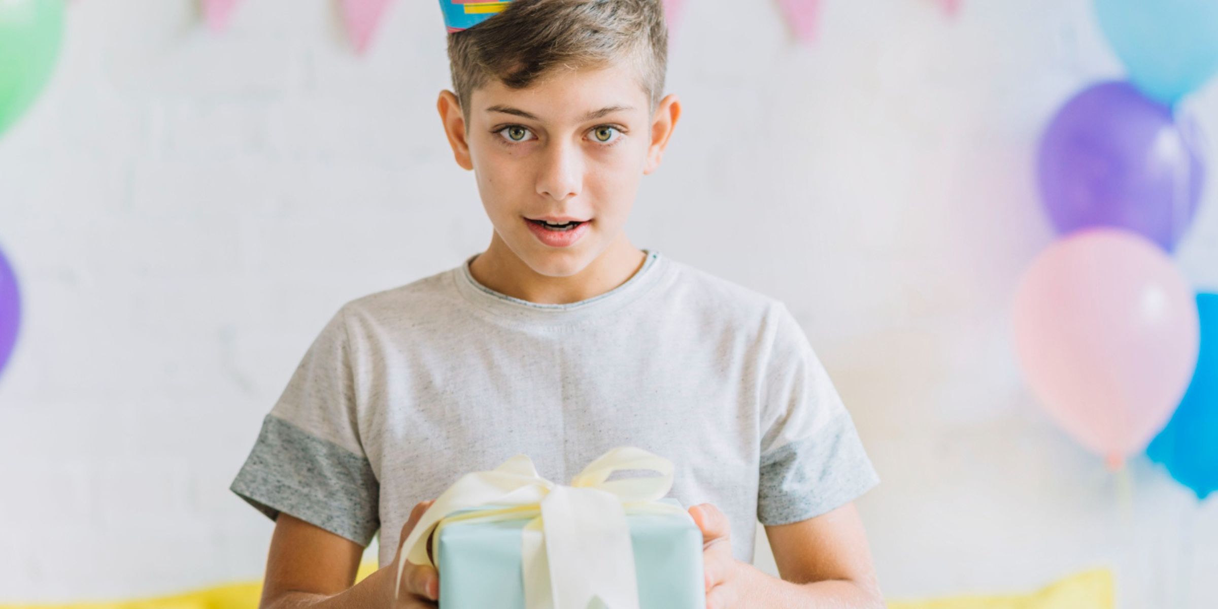 A young boy wearing a party hat and holding a wrapped gift, looking surprised during a birthday celebration | Source: No source