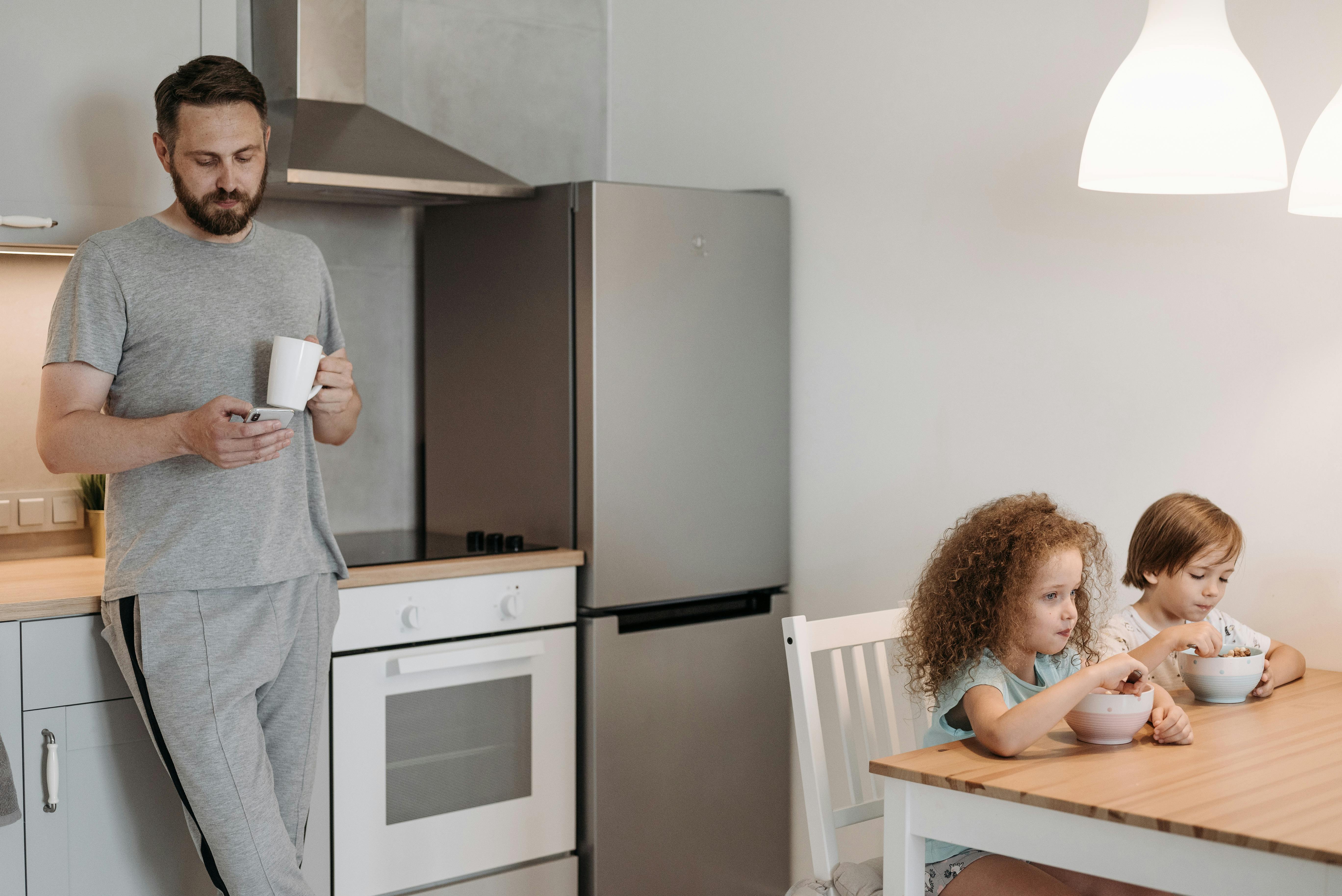 A man using his phone while his children eat | Source: Pexels