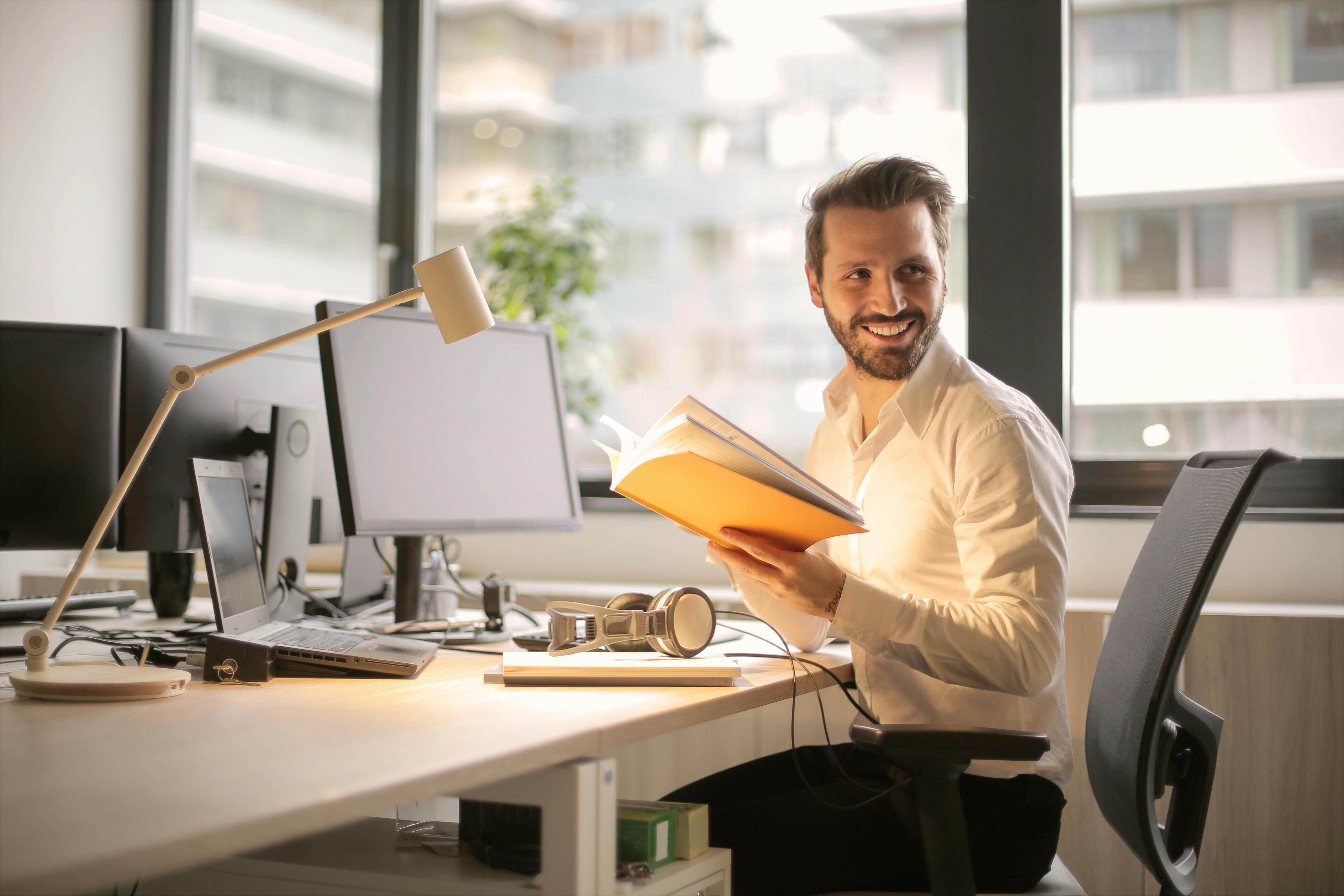 Man holding a book in front of a computer | Source: Pexels