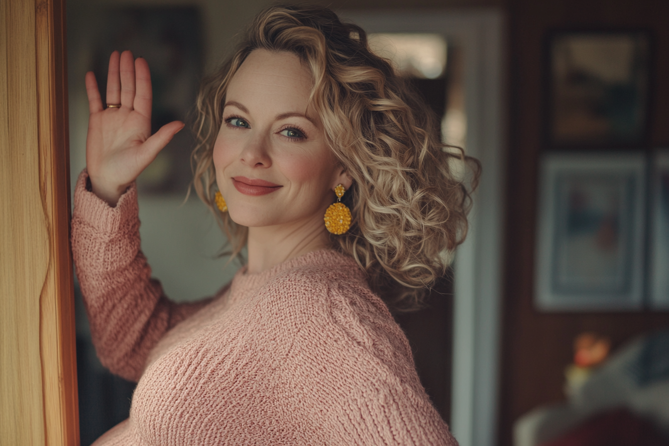 A pregnant woman in her 30s waving goodbye with a small smile | Source: No source