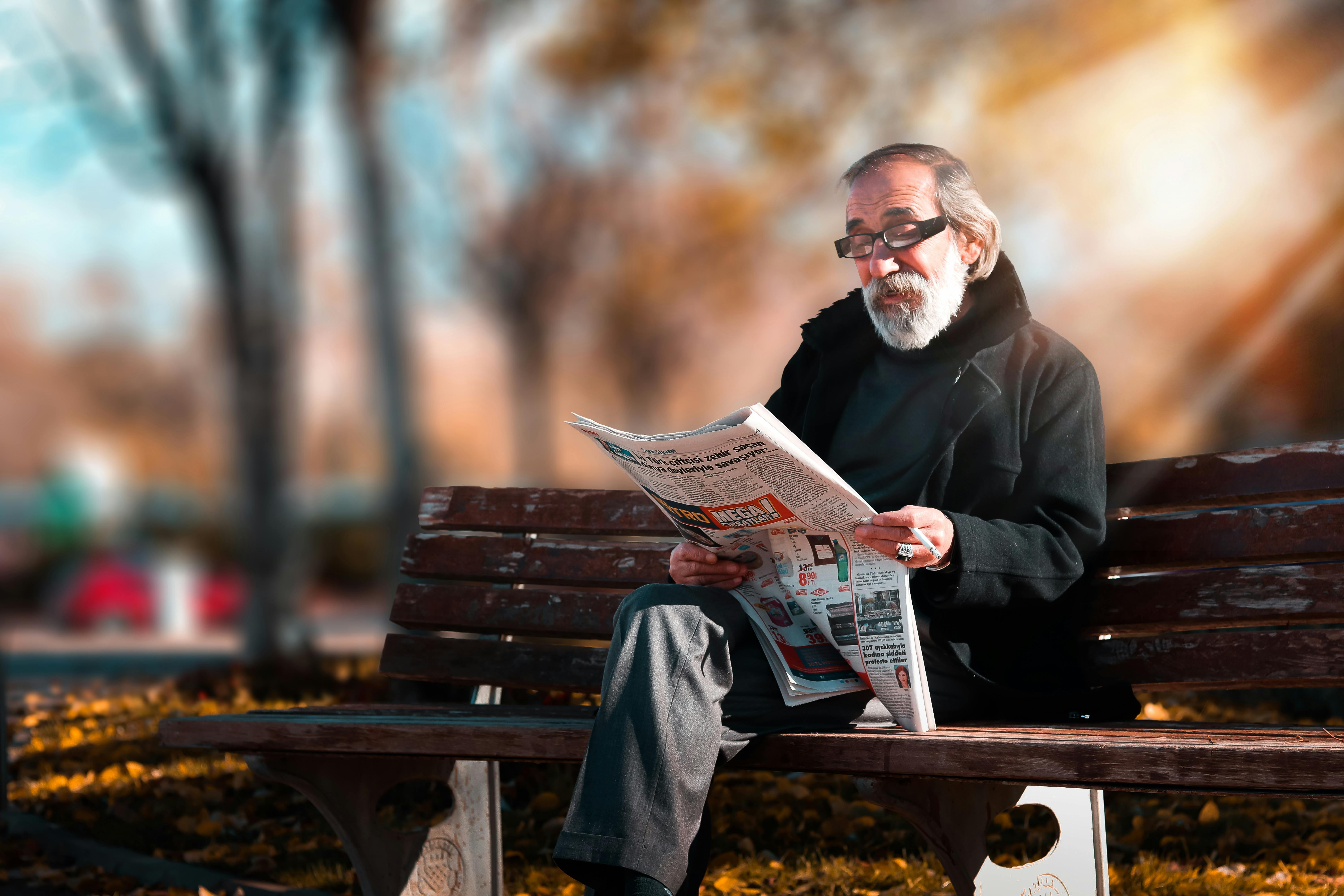 Man on a bench reading a newspaper | Source: Pexels