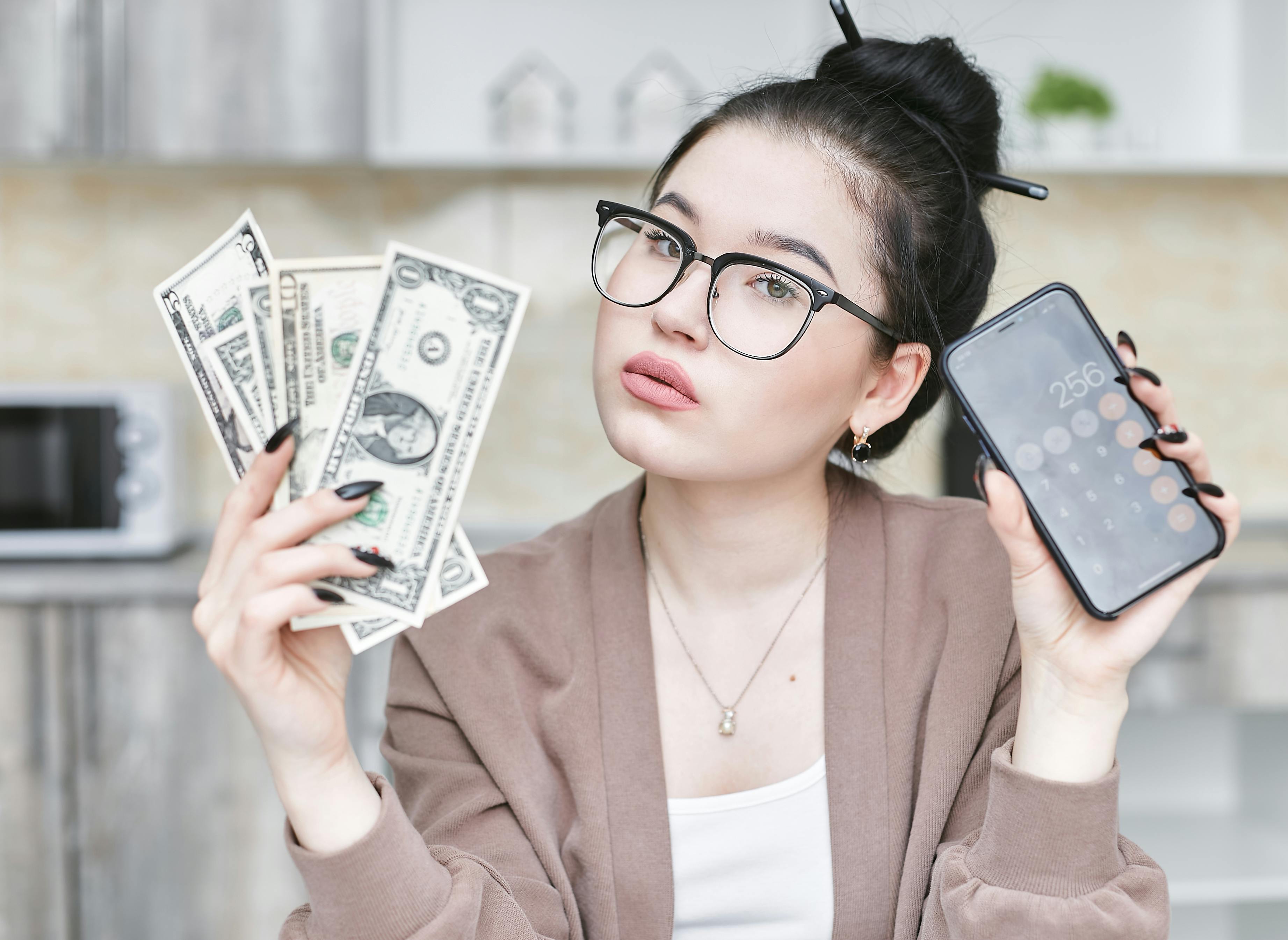 Woman holding money and a smartphone | Source: Pexels