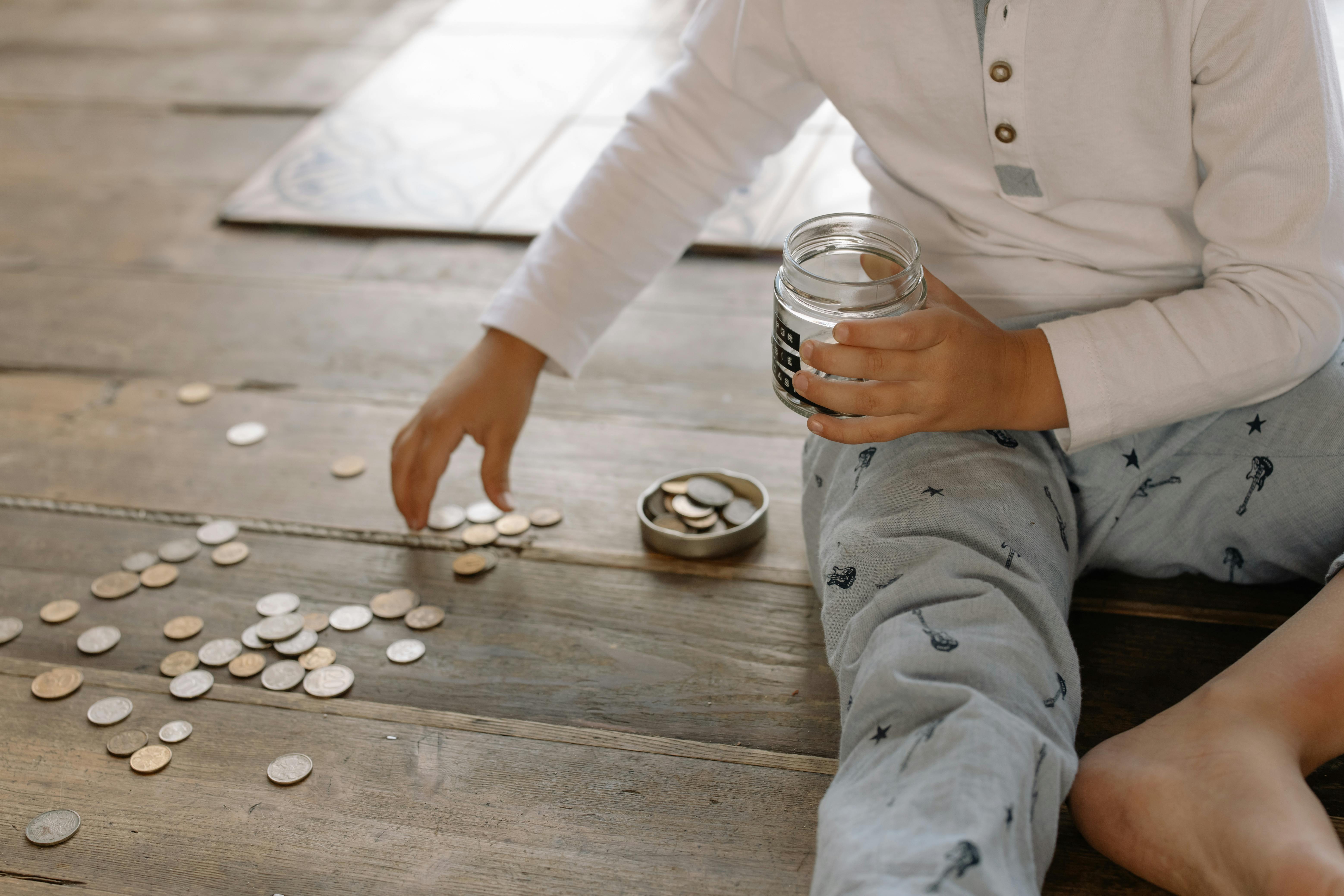 A child sitting on a wooden floor is holding a glass jar | Source: Pexels