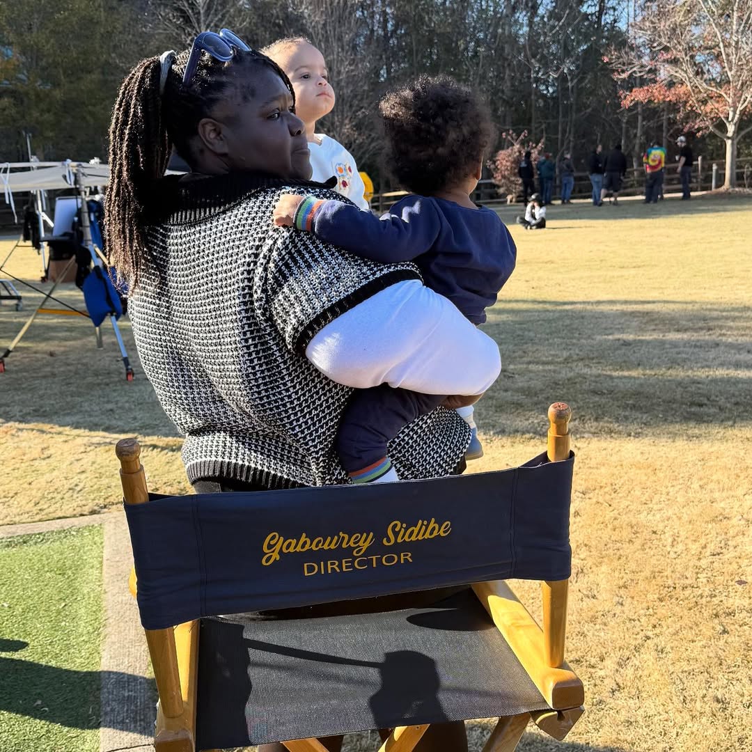 Gabourey Sidibe is seated sideways in her director's chair, cradling both twins — Maya facing outward on her left, Cooper over her shoulder — offering a calm, candid side profile on set. | Source: Instagram/brandontour