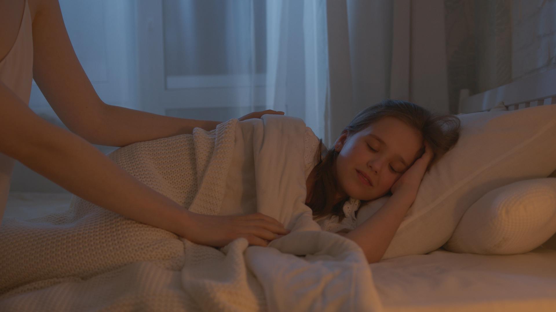A woman tucking a girl into bed | Source: Pexels