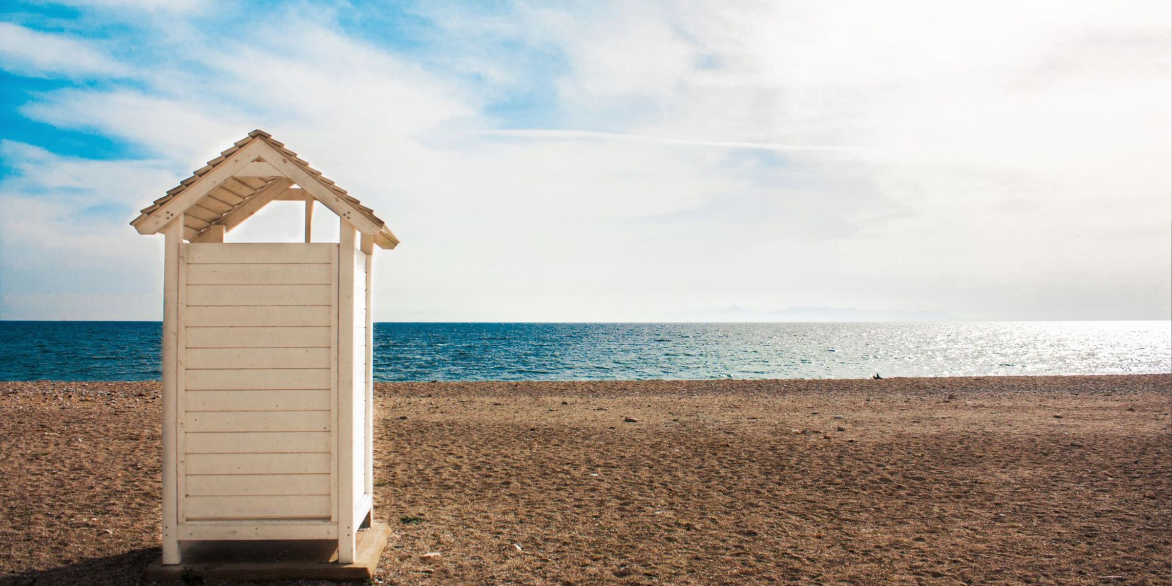 A small wooden beach hut on a quiet sandy shore overlooking the calm sea under a bright sky | Source: Pexels