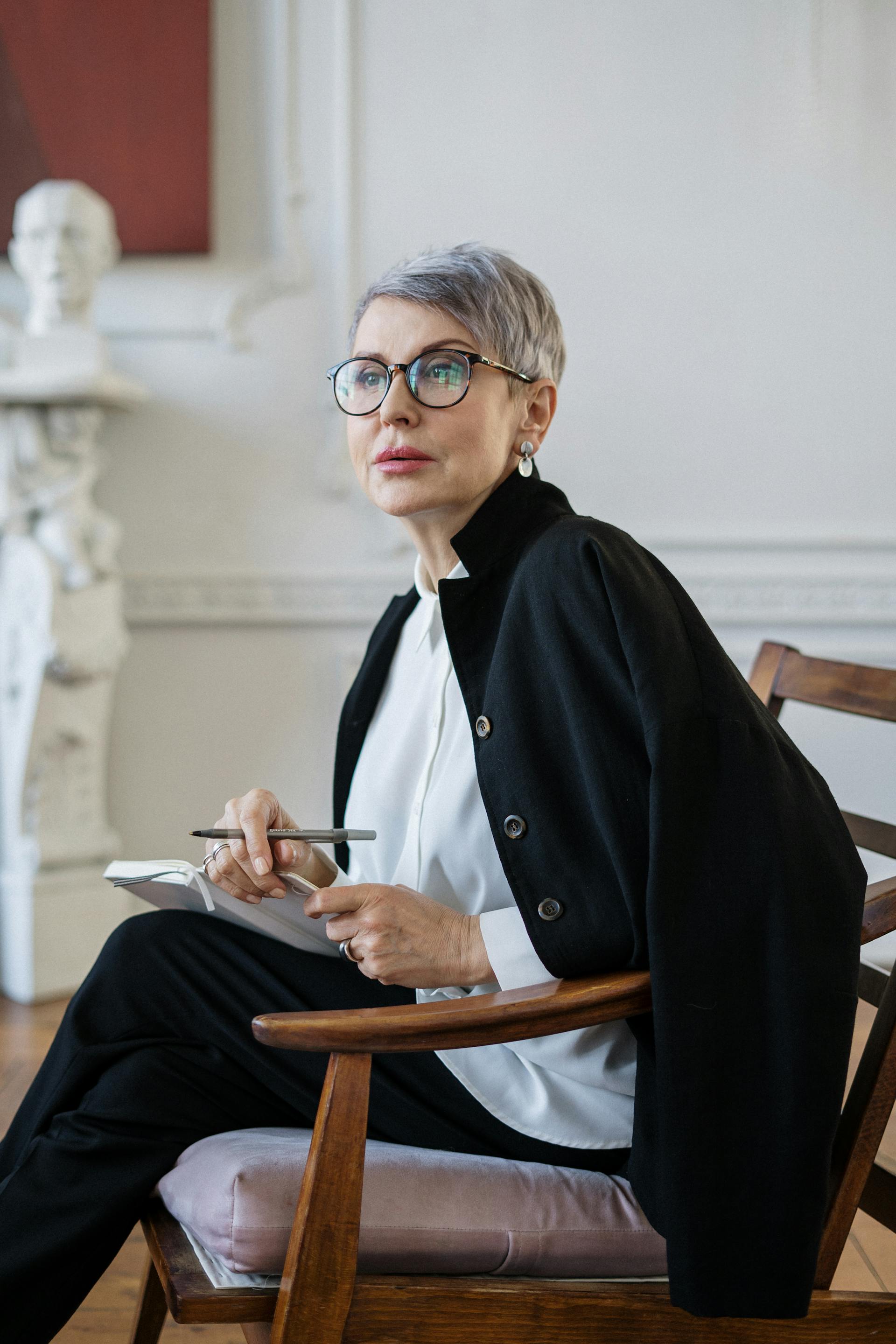 A woman in a black blazer sitting on a wooden chair | Source: Pexels
