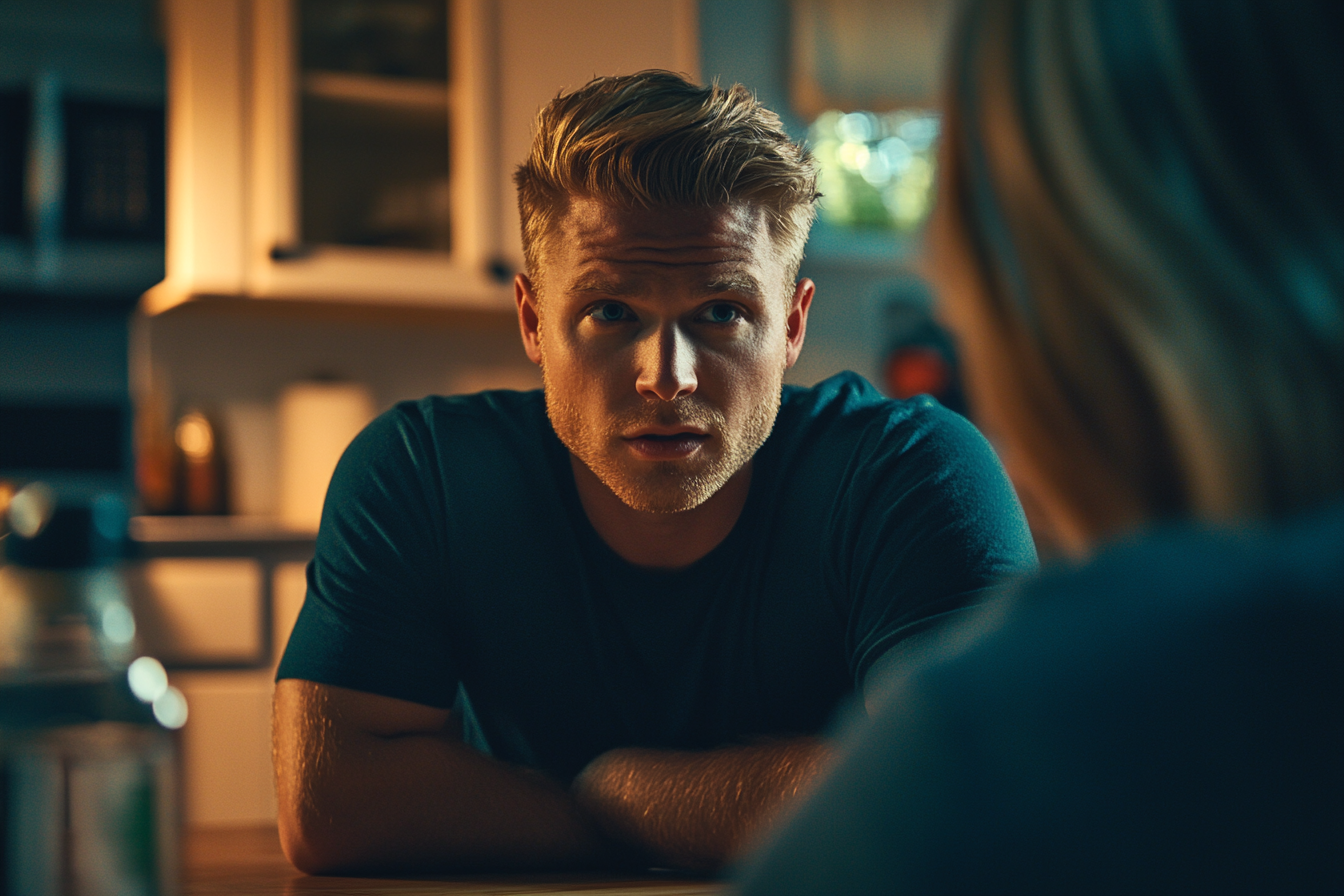 A blonde man in his 30s looking worried while talking to a woman at the kitchen table | Source: no source