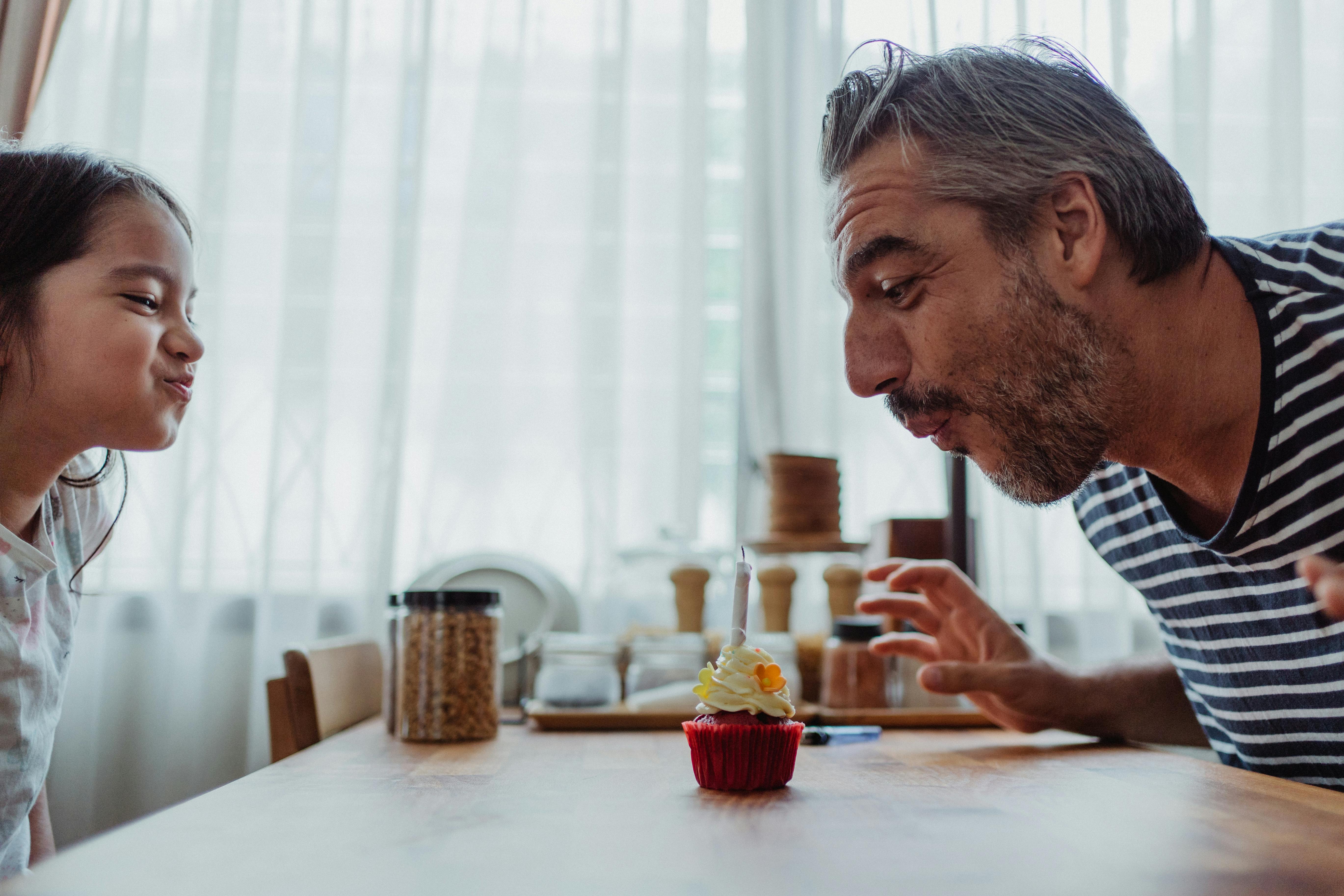 A man and a little girl blowing at a candle on a cupcake | Source: Pexels