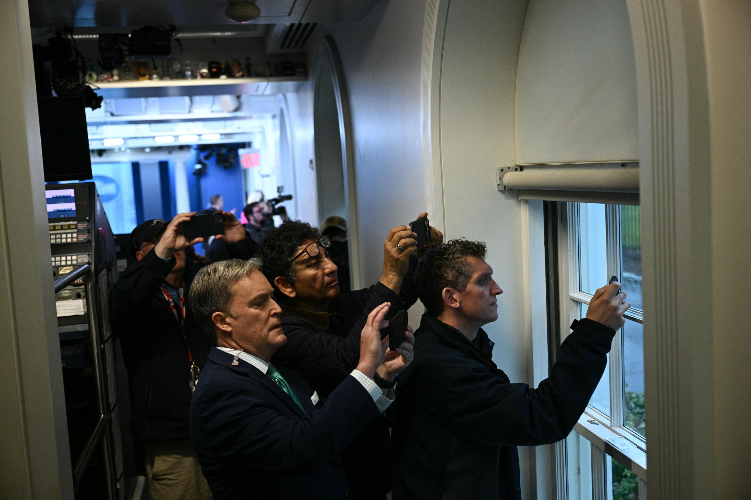 Reporters hold up their phones near a window in the Press Briefing room after a lockdown was triggered at the White House in Washington, D.C., on May 23, 2026. | Source: Getty Images