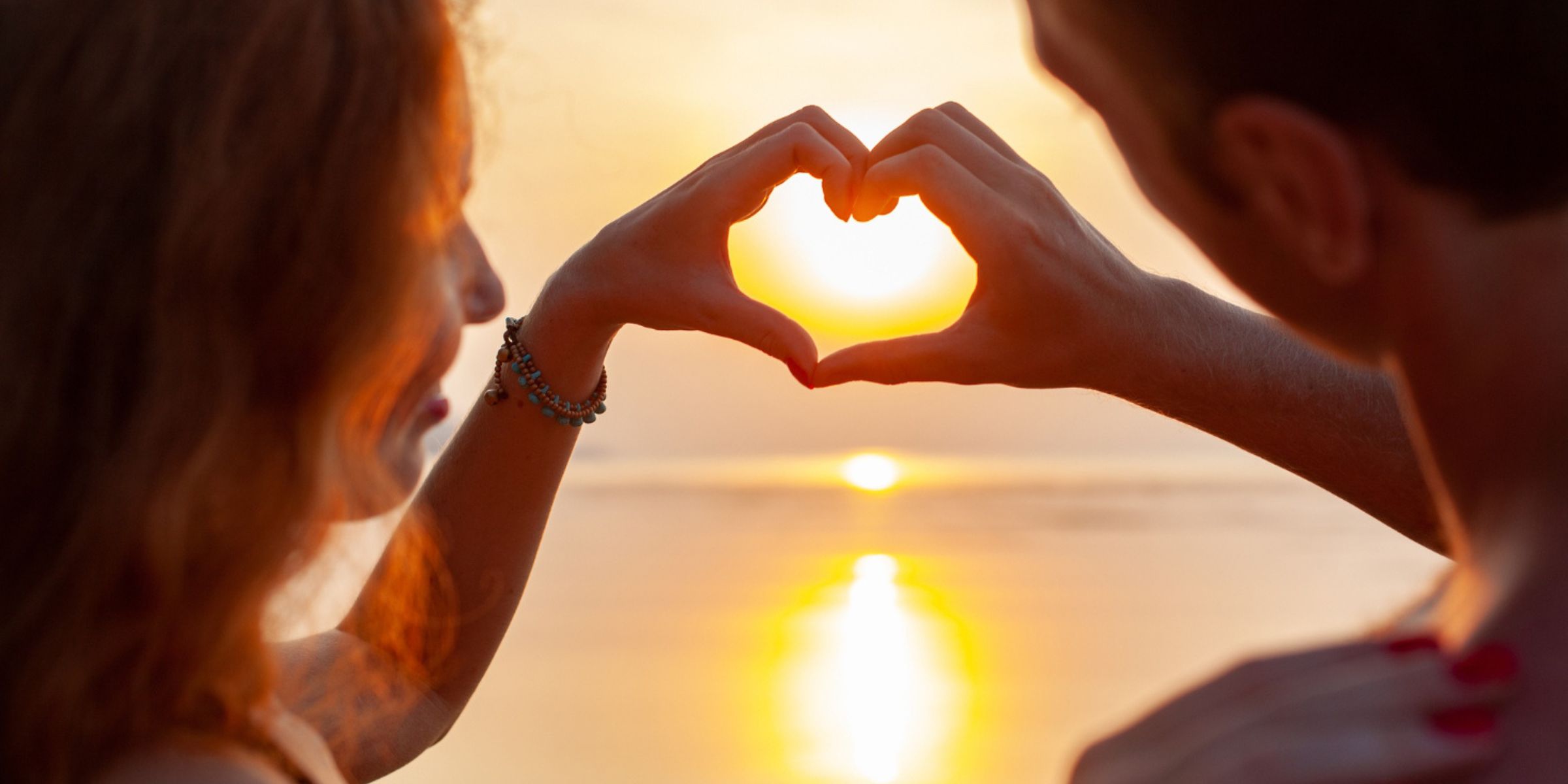 A couple forming a heart shape with their hands while watching the sunset | Source: No source