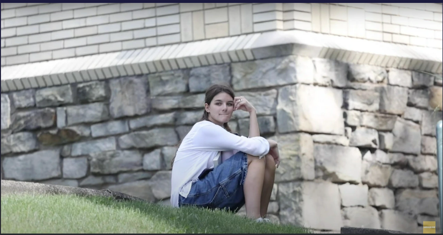 Suri Cruise sits peacefully on a grassy slope, lost in a quiet moment of thought. The soft light and serene backdrop mirror her calm, reflective expression. It’s a candid glimpse of youthful grace. | Source: YouTube/PageSix