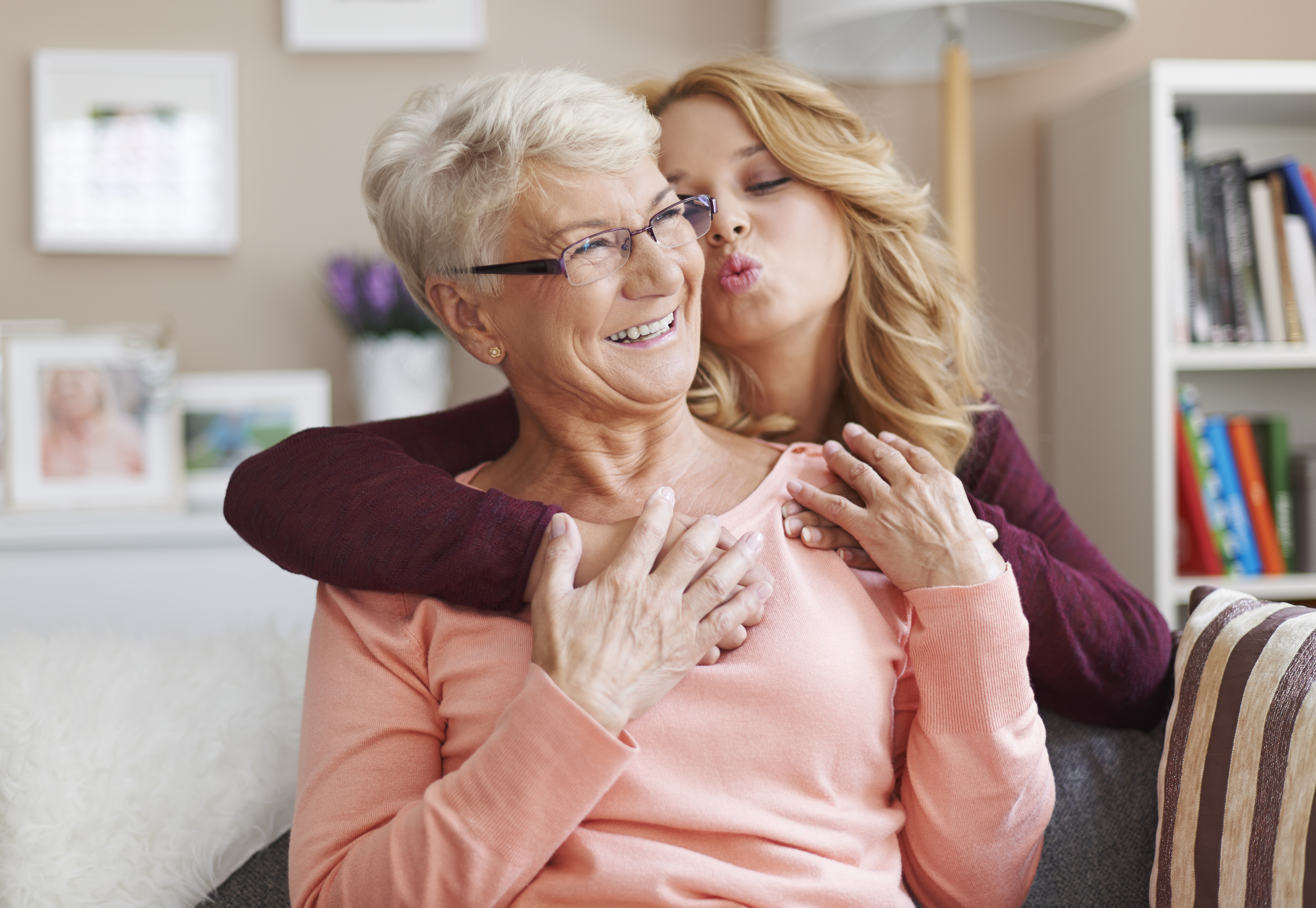 Teen girl hugging her smiling grandmother from behind and attempting to kiss her | Source: Freepik